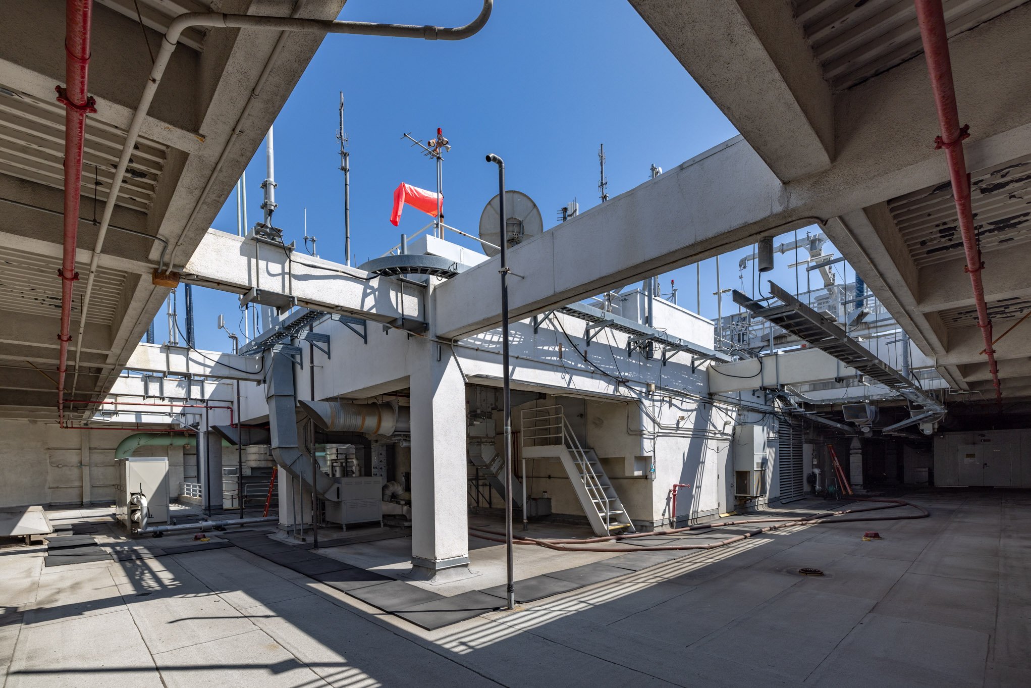 Rooftop of a building with HVAC units, antennas, and pipes under a clear blue sky.