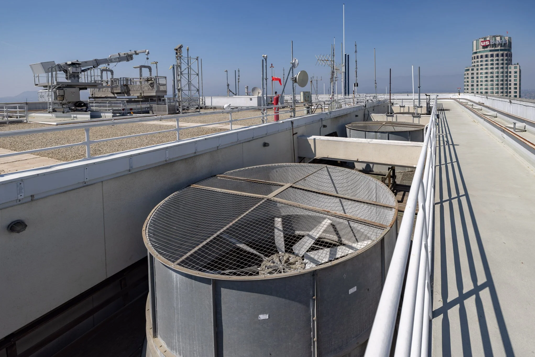 Rooftop with various antennas, satellite dishes, and large air conditioning units in an urban city skyline.