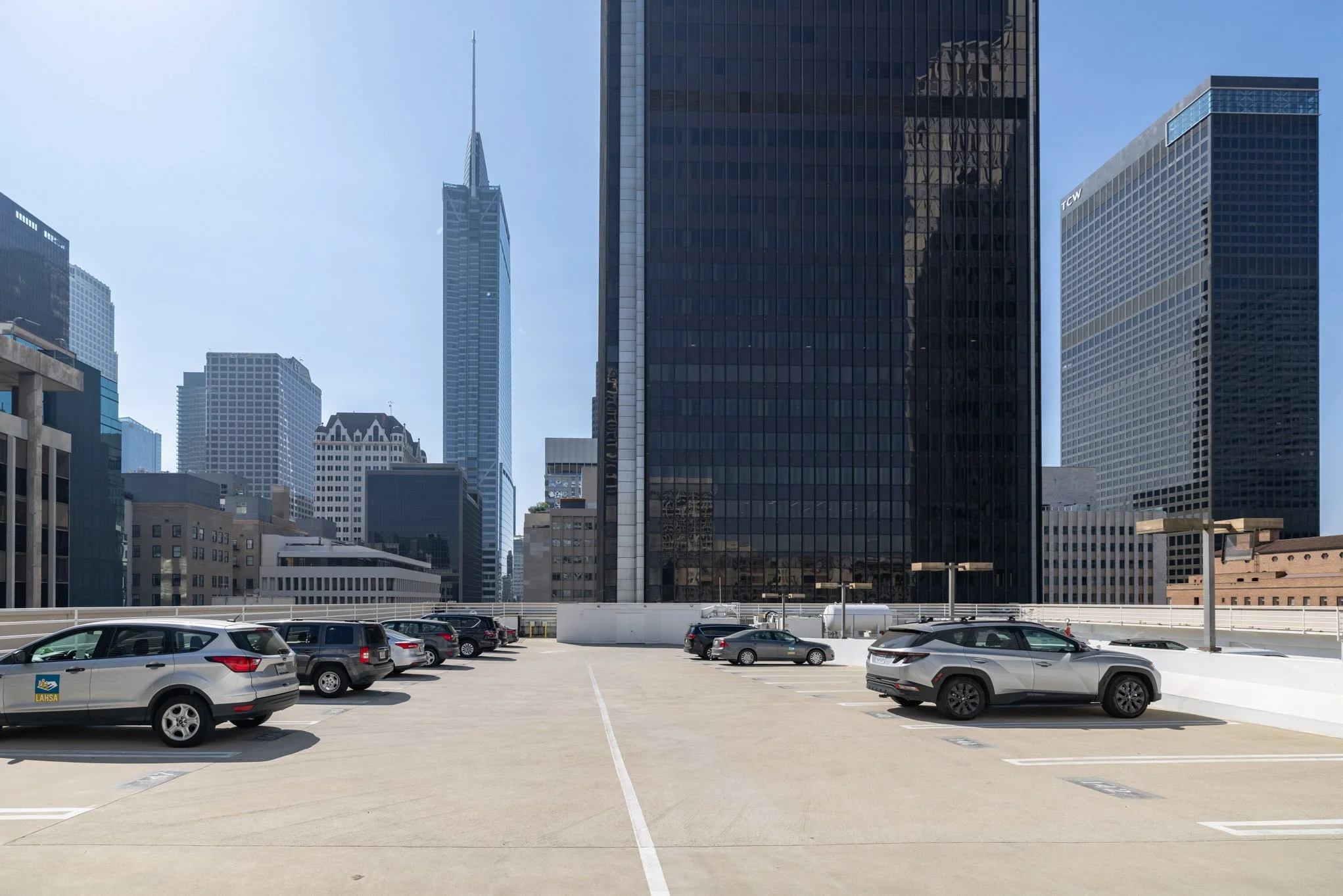 Empty rooftop parking lot with several parked cars and tall skyscrapers in the background.
