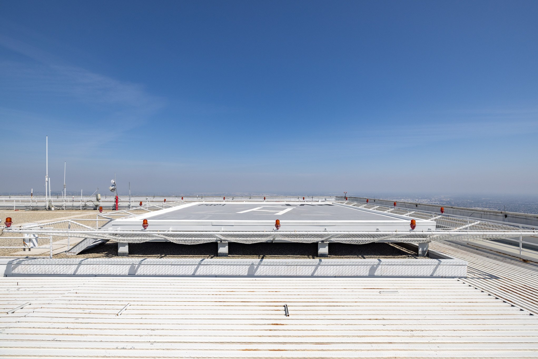 Rooftop helipad with clear blue sky and horizon in the background.