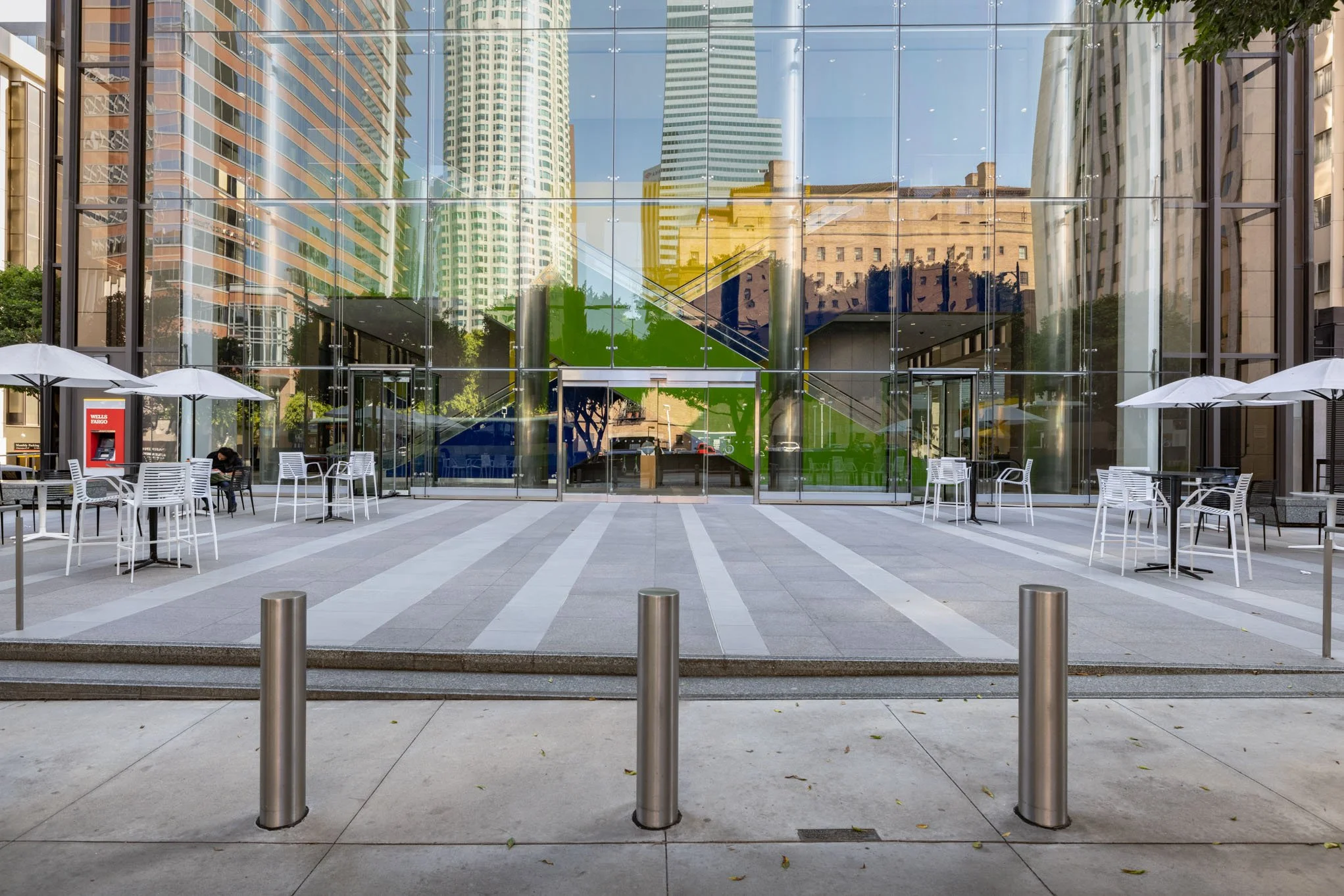 Empty outdoor seating area with white tables and umbrellas in front of a modern glass building reflecting tall skyscrapers.