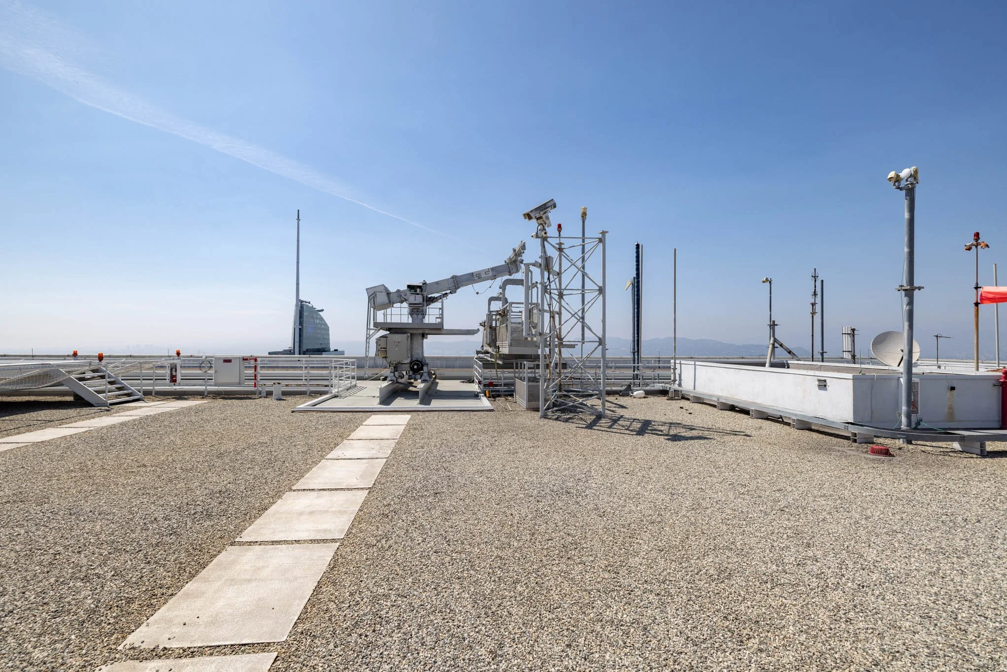 Rooftop with antennas, cameras, and equipment under a clear blue sky with the cityscape in the background.