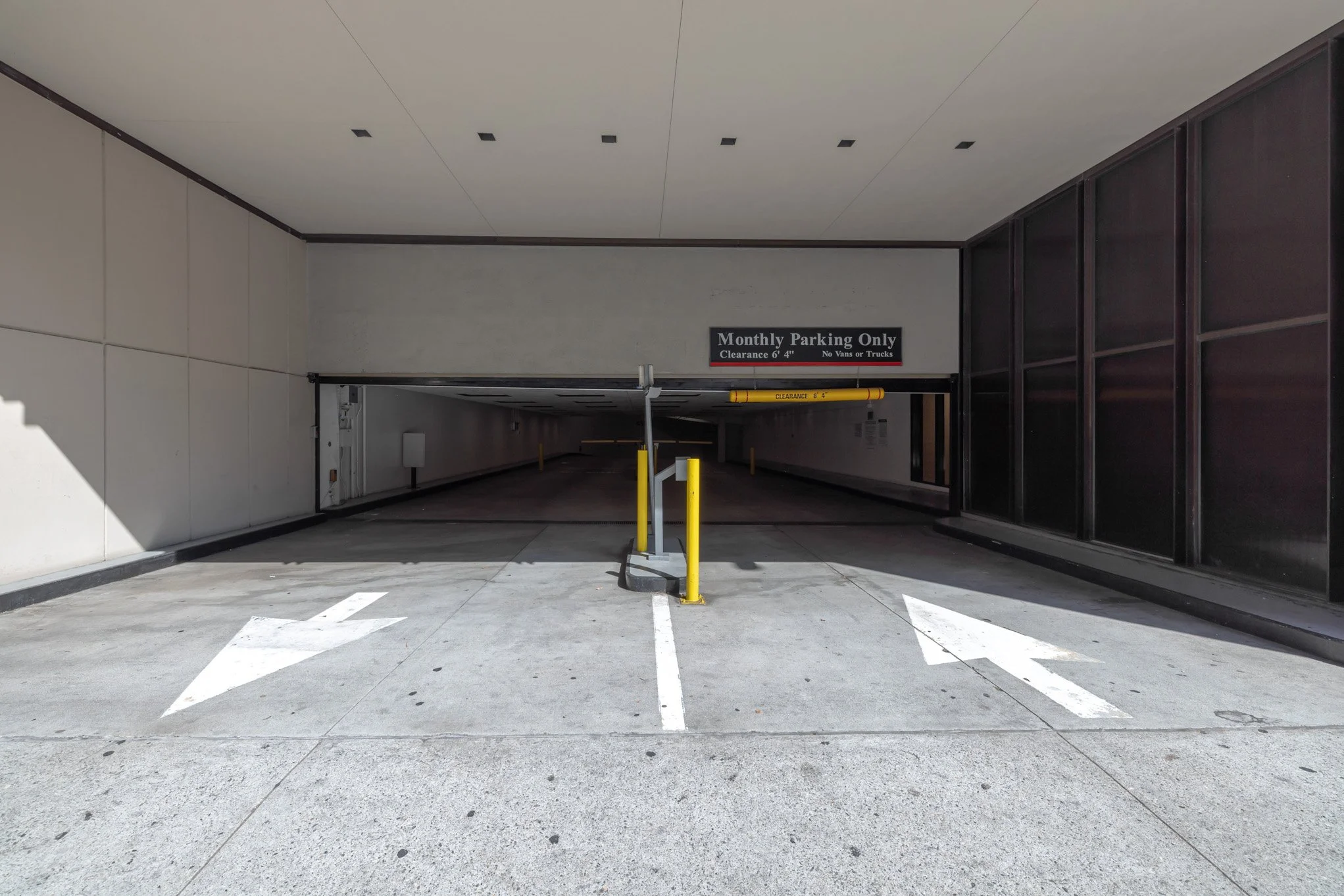 Underground parking entrance with a white arrow pointing left, a yellow pole gate, and a sign indicating 'Monthly Parking Only' with a 6-foot 4-inch clearance.