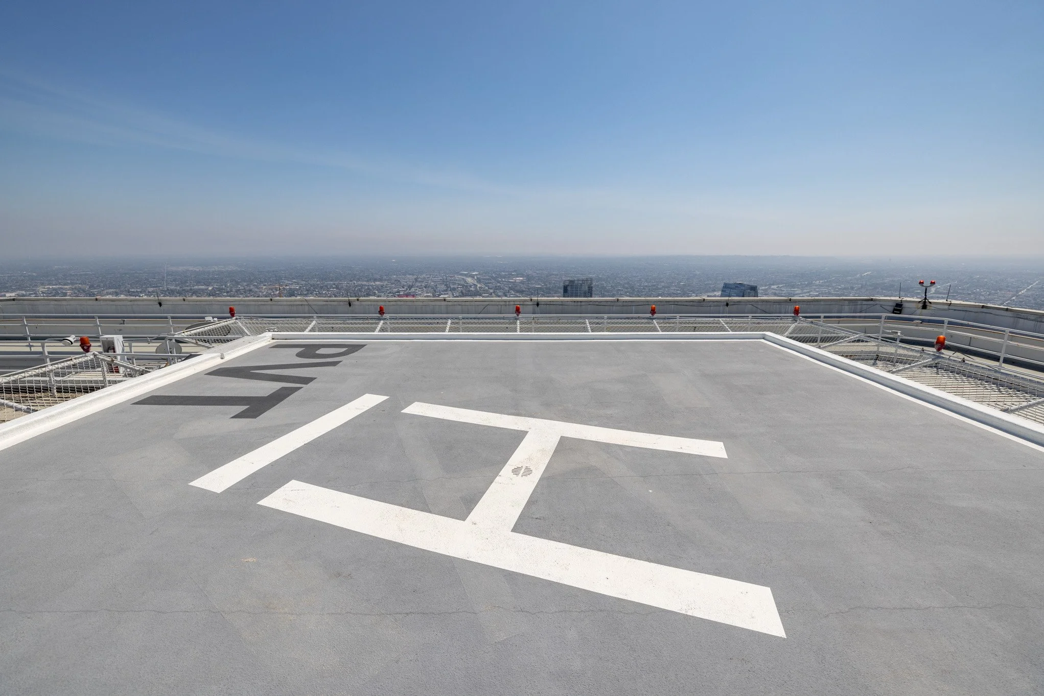 Helipad on top of a building with a city view in the background, marked with the letter 'H' and white lines.