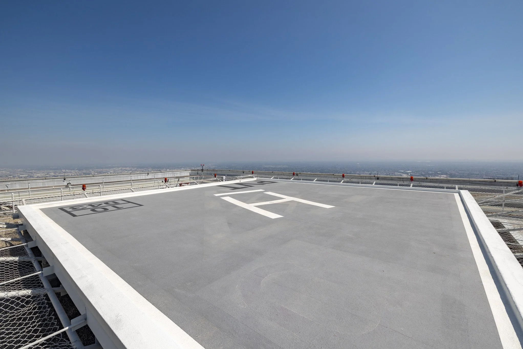 Helipad on top of a tall building with a city view in the distance under a clear blue sky.