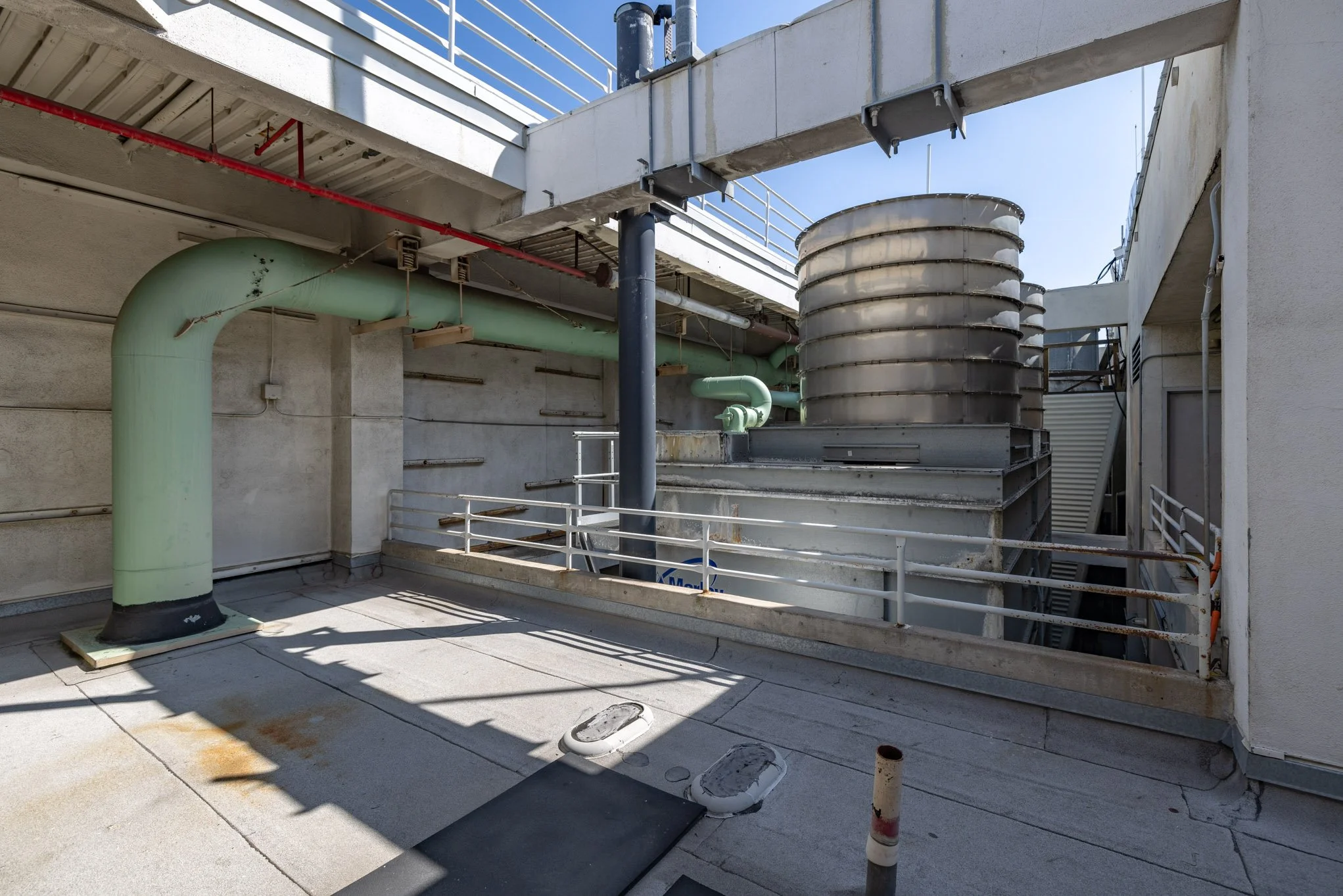 Rooftop with large green and metal industrial ventilation pipes and a staircase, part of a building's ventilation system.