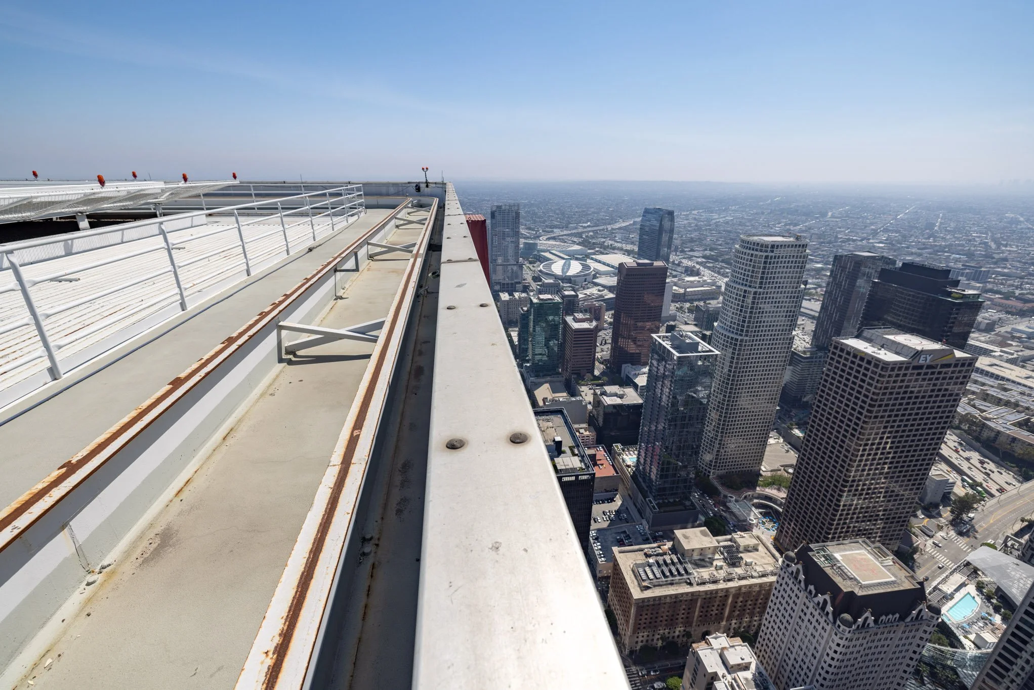View from the top of a skyscraper looking down at the city skyline, with high-rise buildings and streets below, under a clear blue sky.