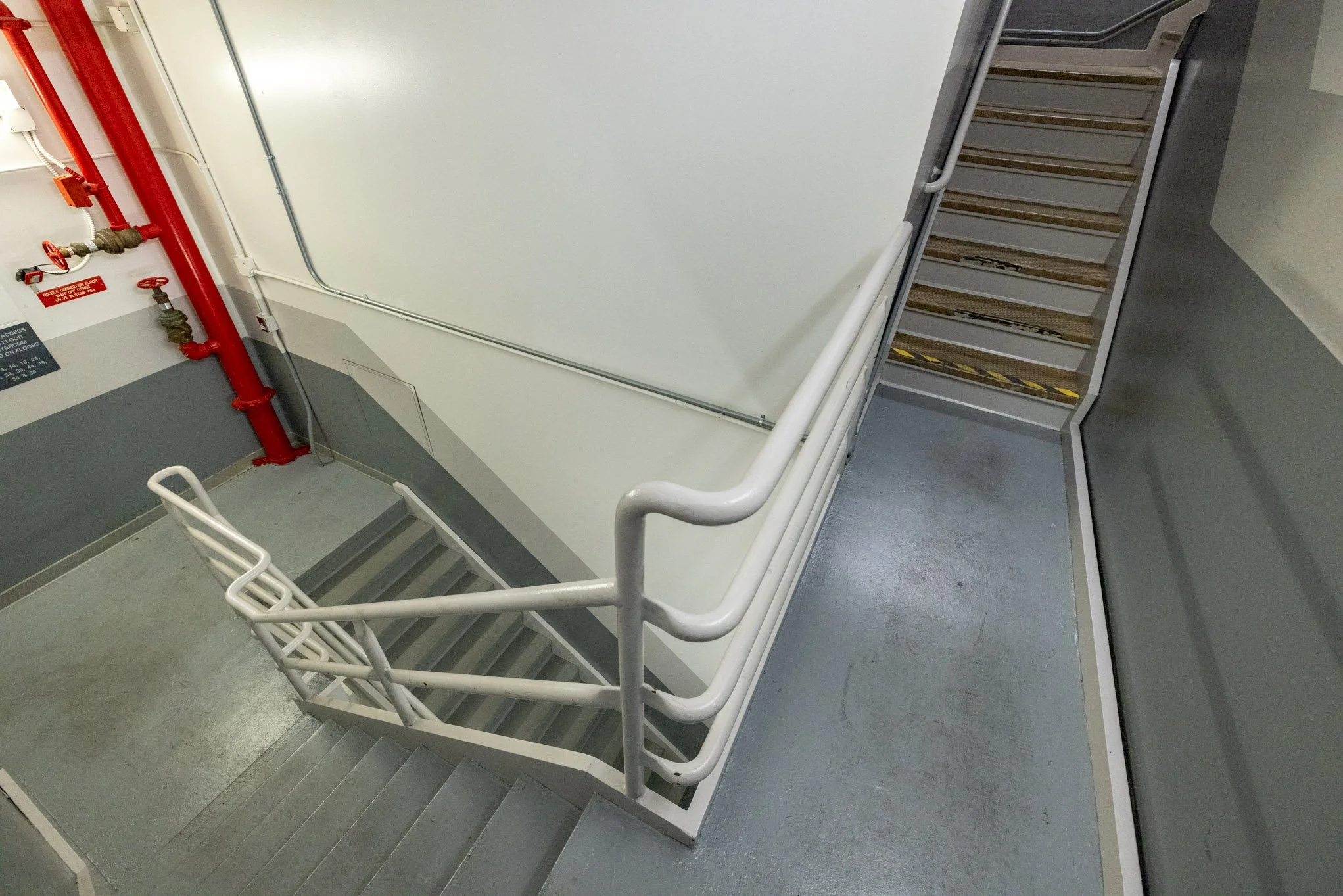 Indoor staircase with gray steps, white railings, and a fire safety system with red pipes and valves.
