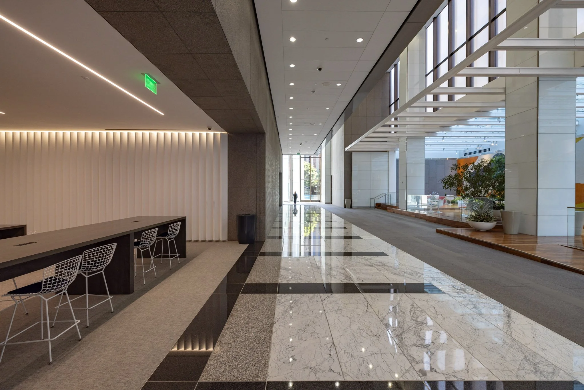Modern indoor lobby with marble flooring, seating area, large windows, and plants near the entrance.