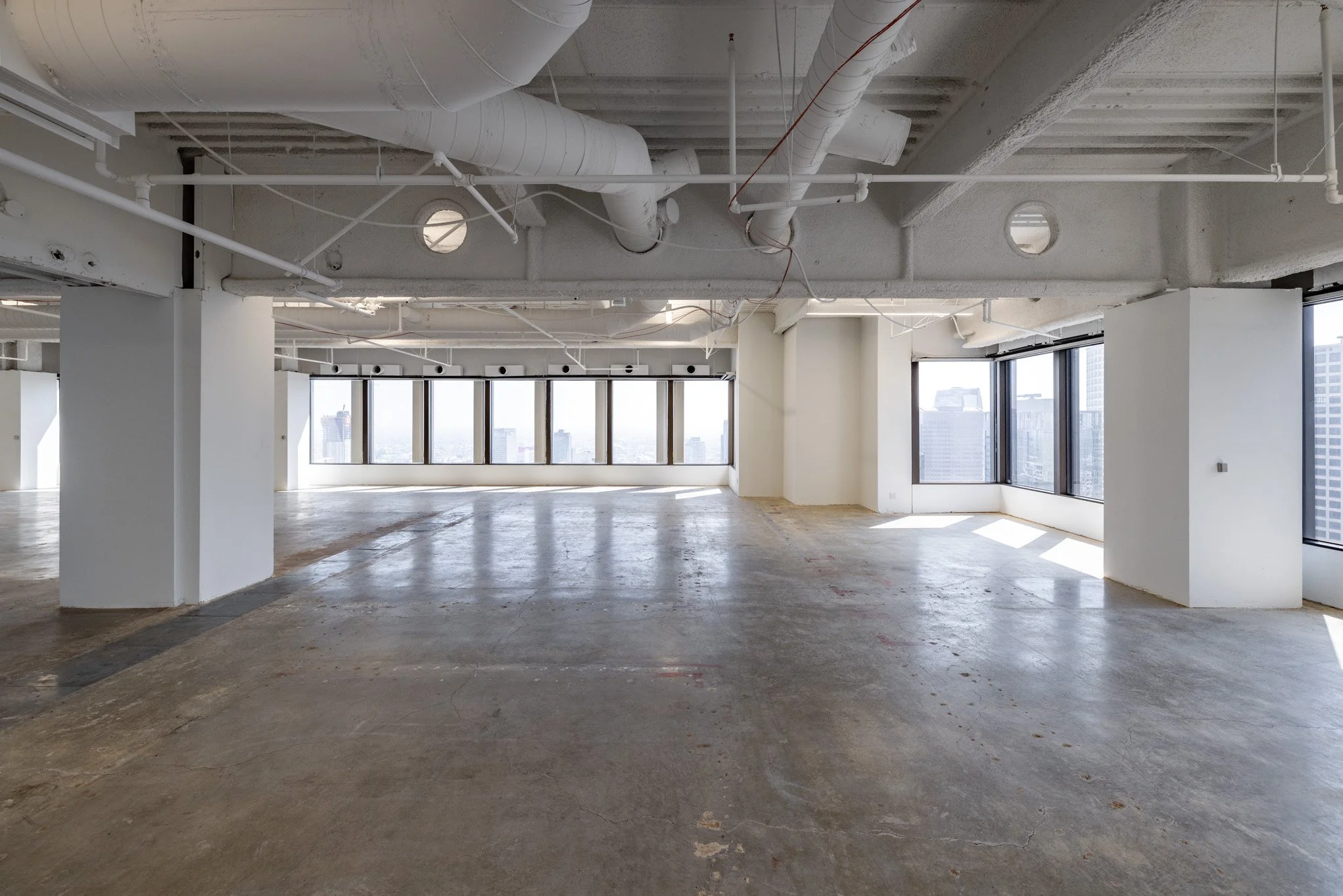 Empty, unfinished interior space of a high-rise building with large windows, white walls, exposed ceilings, and concrete floors.