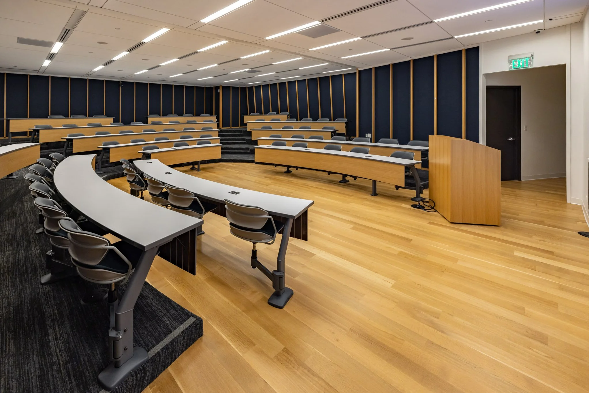 Empty modern lecture hall with tiered seating, wooden floors, and a podium.