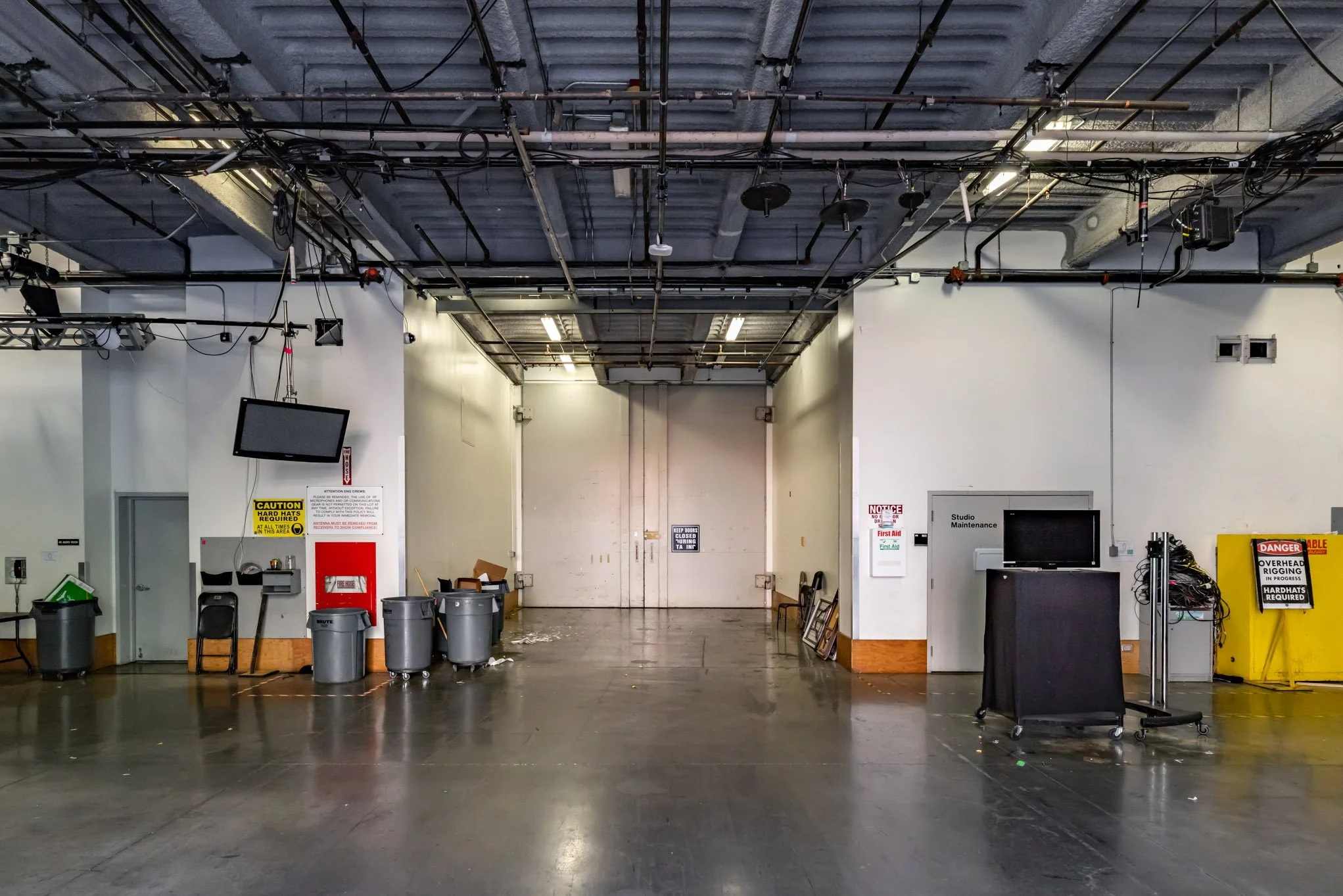 Empty industrial or warehouse space with signs, trash bins, and equipment along the walls.