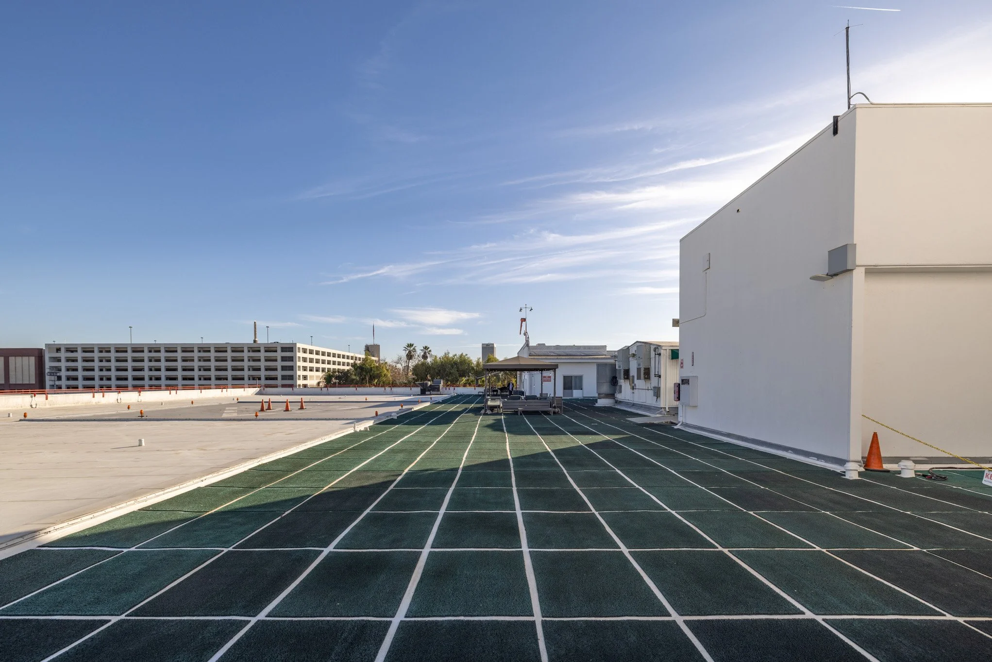 Rooftop parking lot with a green running track, white grid lines, and a white building on the right, under a clear blue sky.