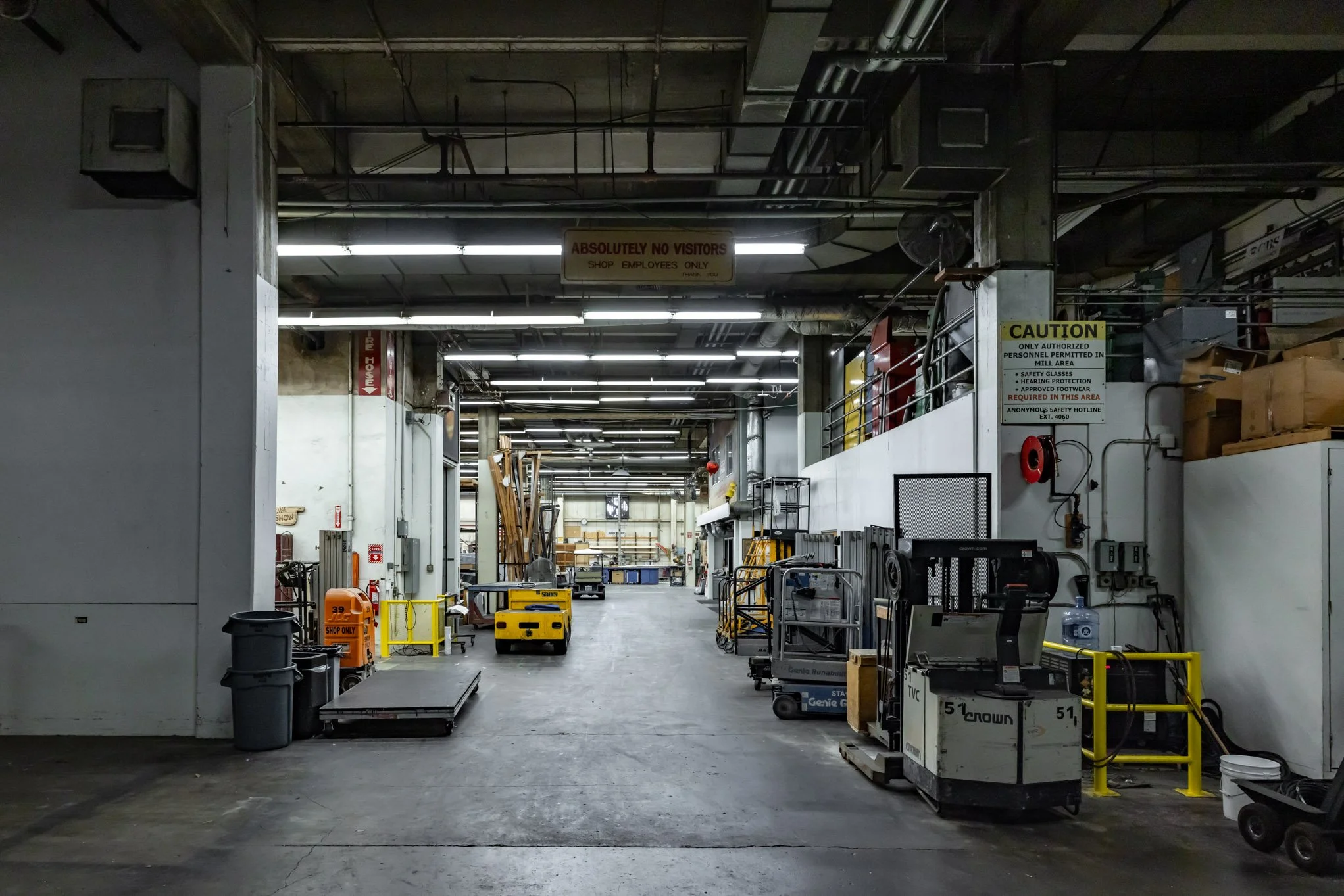 Industrial warehouse aisle with carts, equipment, and stacked boxes, with signs indicating authorized personnel only and safety precautions.