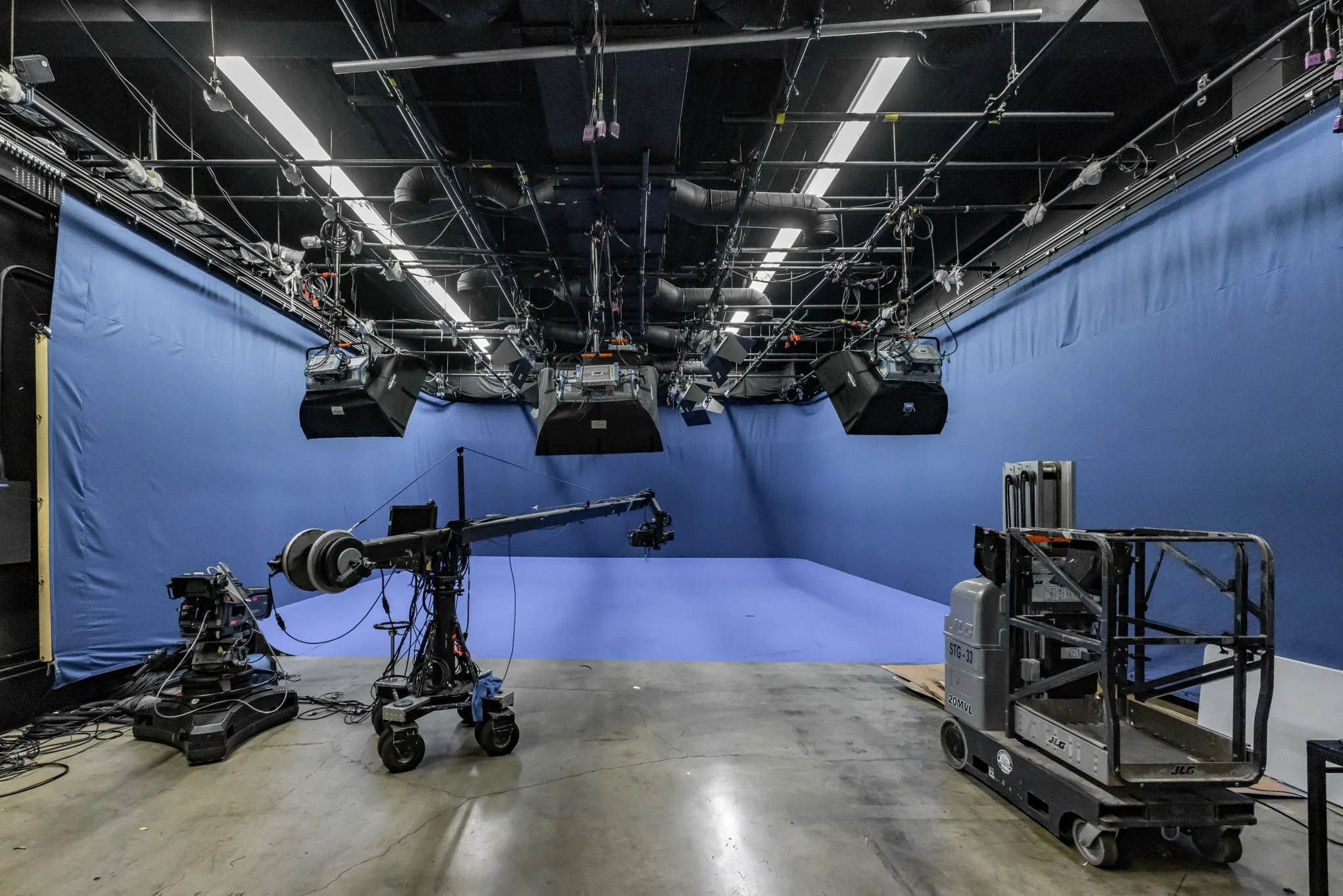 Studio with blue backdrop, camera crane, lighting, and scaffolding equipment.