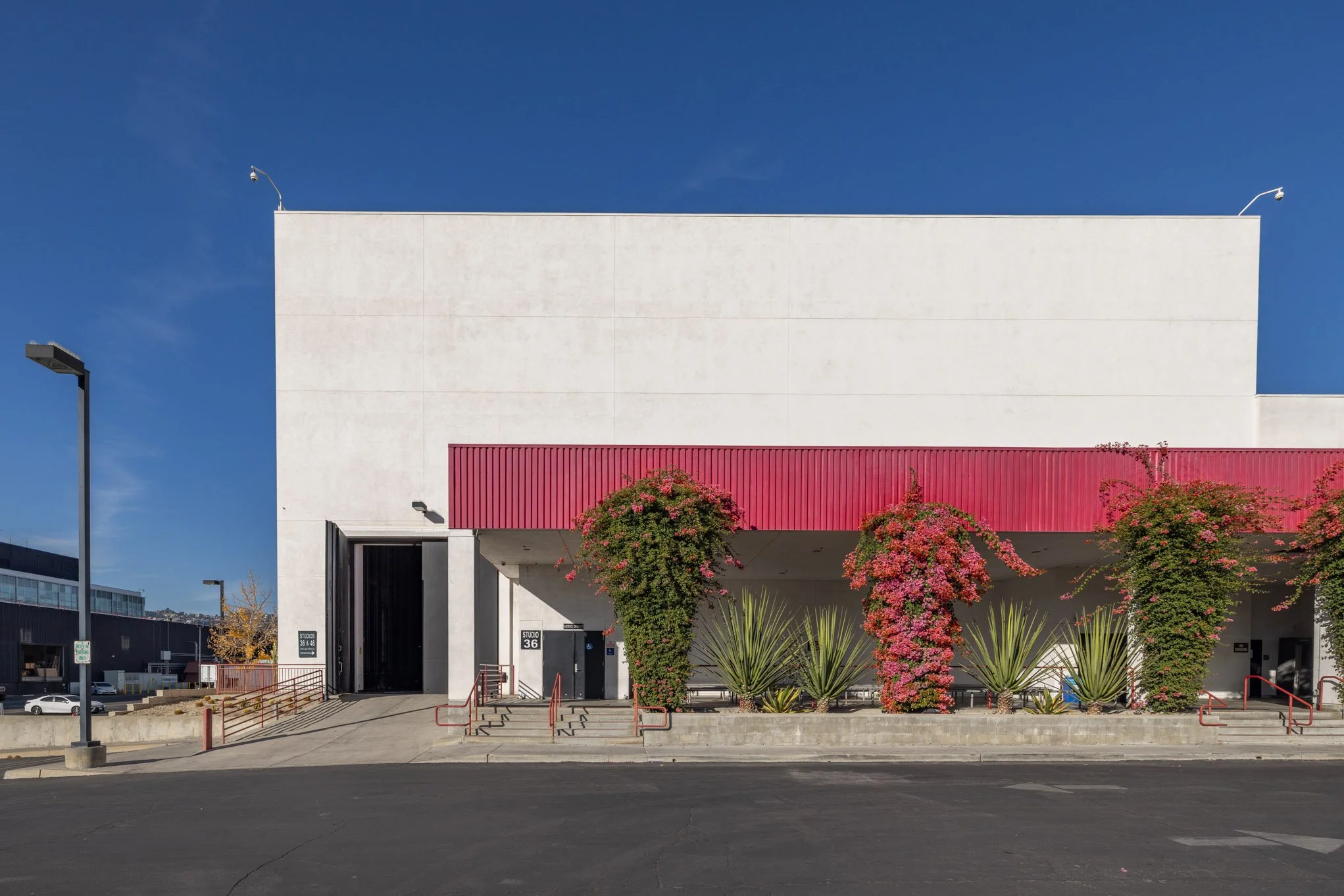 A modern white building with red accents and pink flowering plants in front, against a clear blue sky.