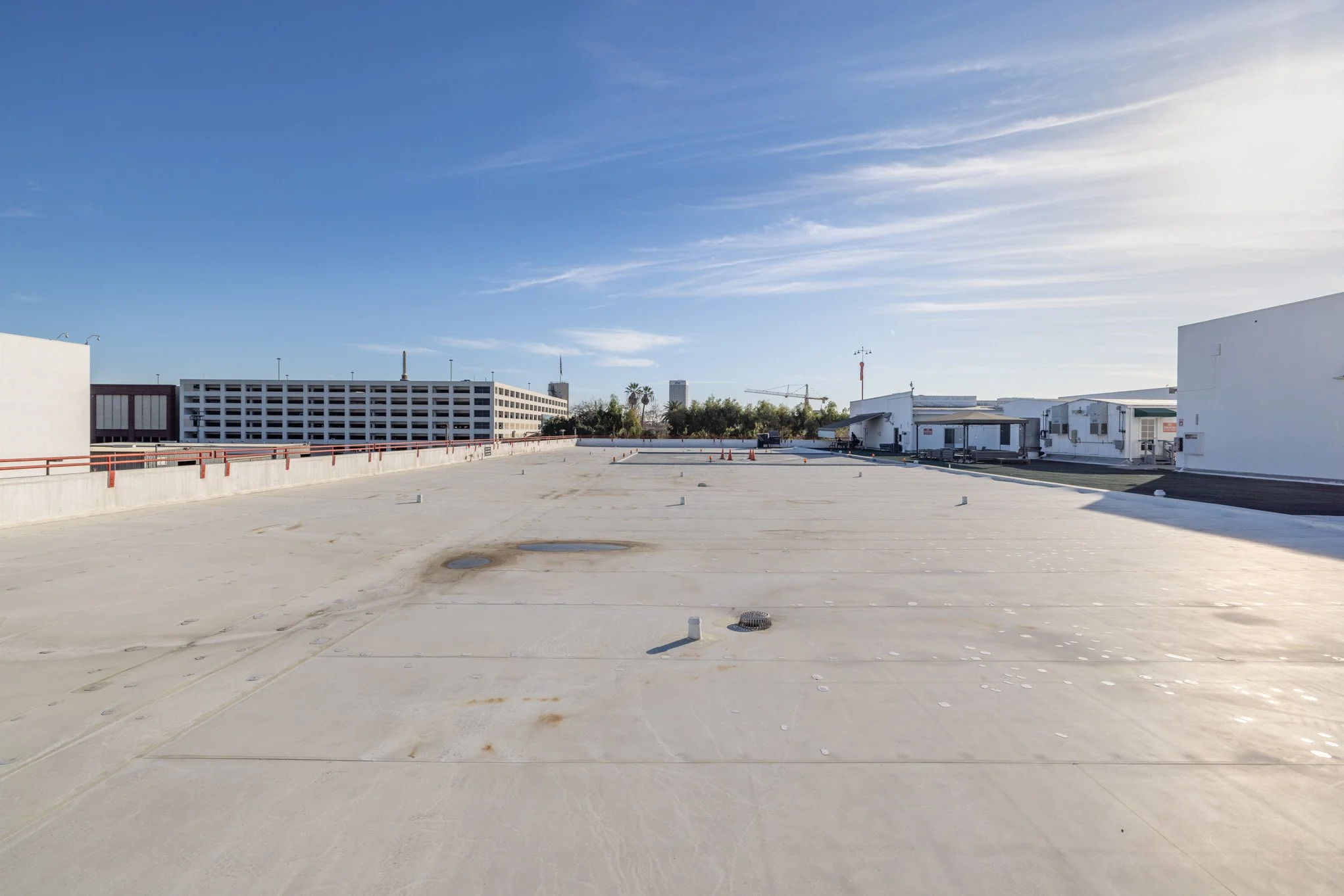 Empty rooftop parking lot with building structures in the background, under clear blue sky.