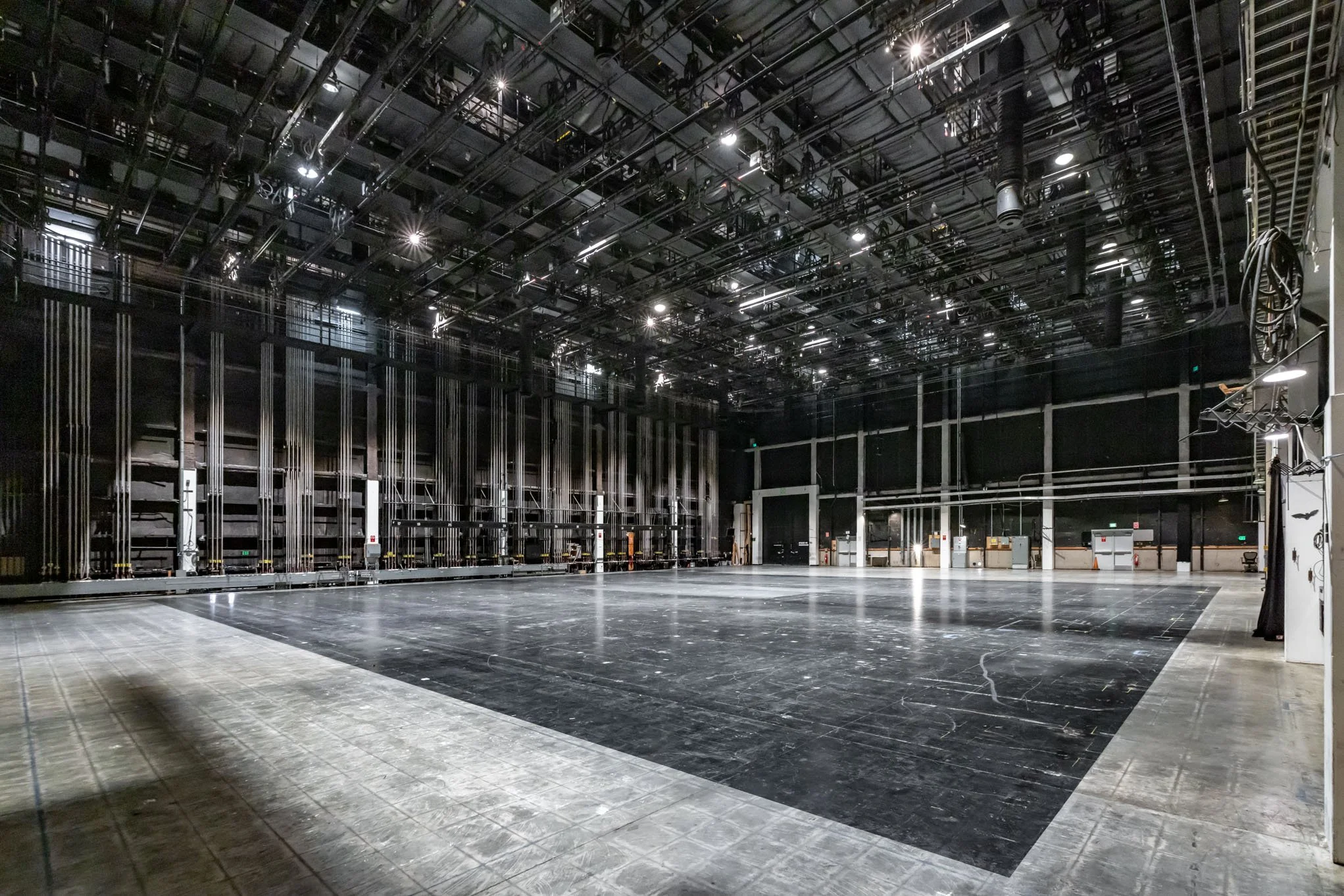 Empty black stage area in a theater or studio with professional lighting and rigging overhead.