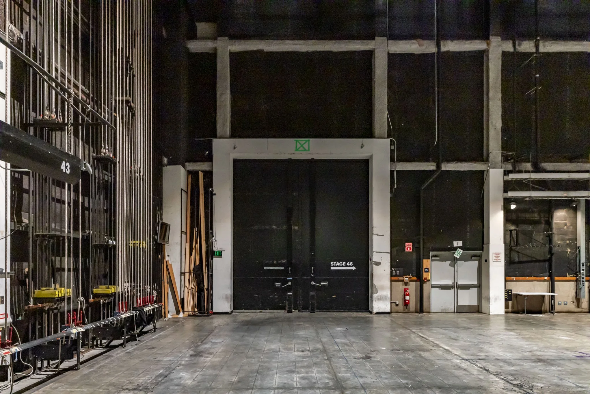 Backstage area of a theater with black stage doors labeled 'Stage 46', stage equipment, and storage on the left.