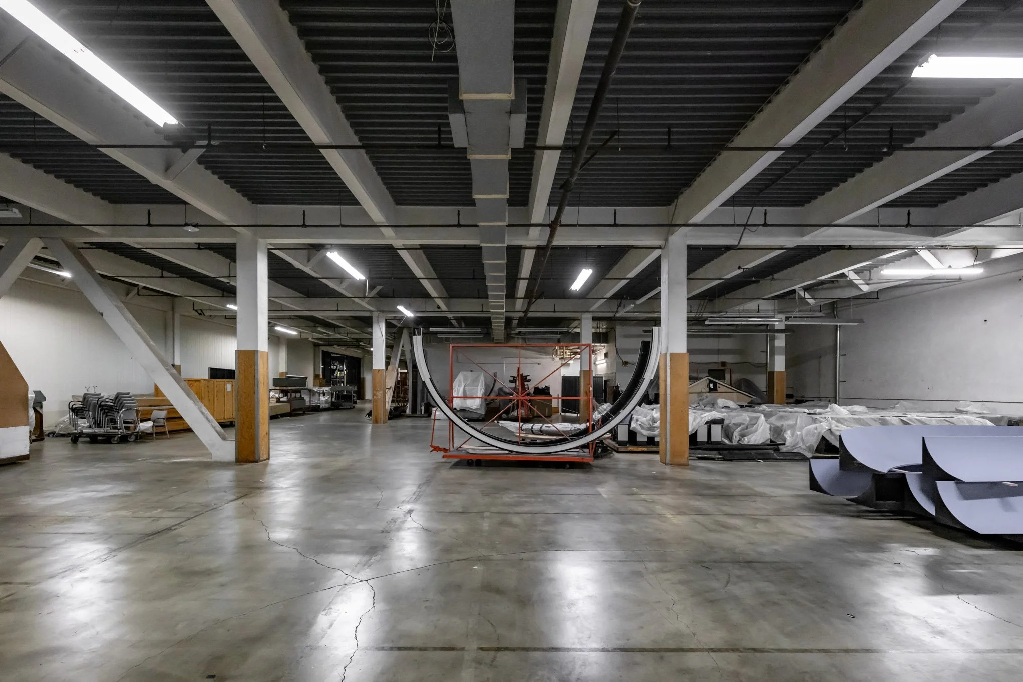 Empty commercial or industrial space with construction materials and equipment, unfinished ceiling, concrete floor, and various stored items.