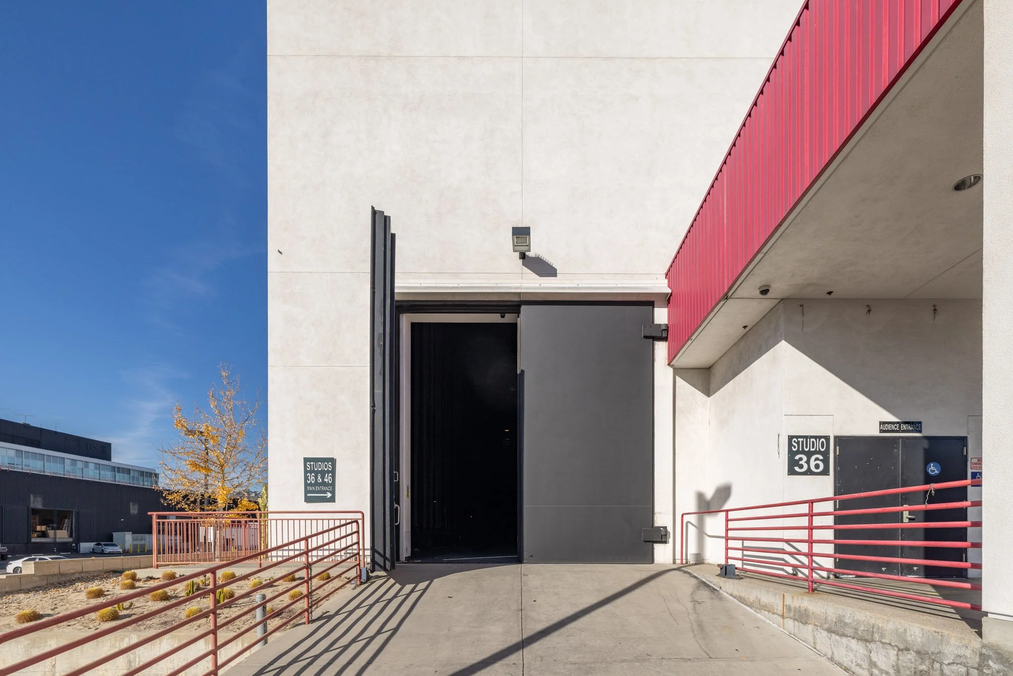 Exterior view of a modern building with black and red accents, open garage door, and signs indicating studio numbers 36 and 46, with a wheelchair accessible entrance.