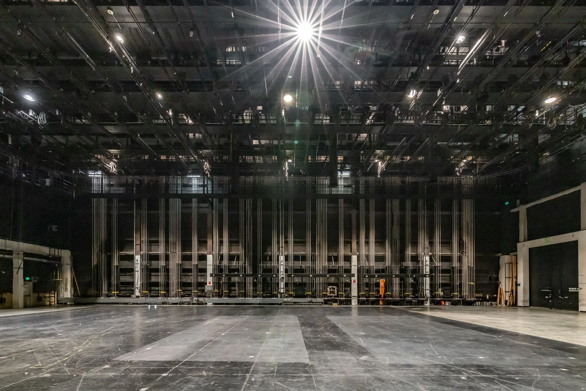 An empty theater stage with visible rigging and lighting, ready for a performance.
