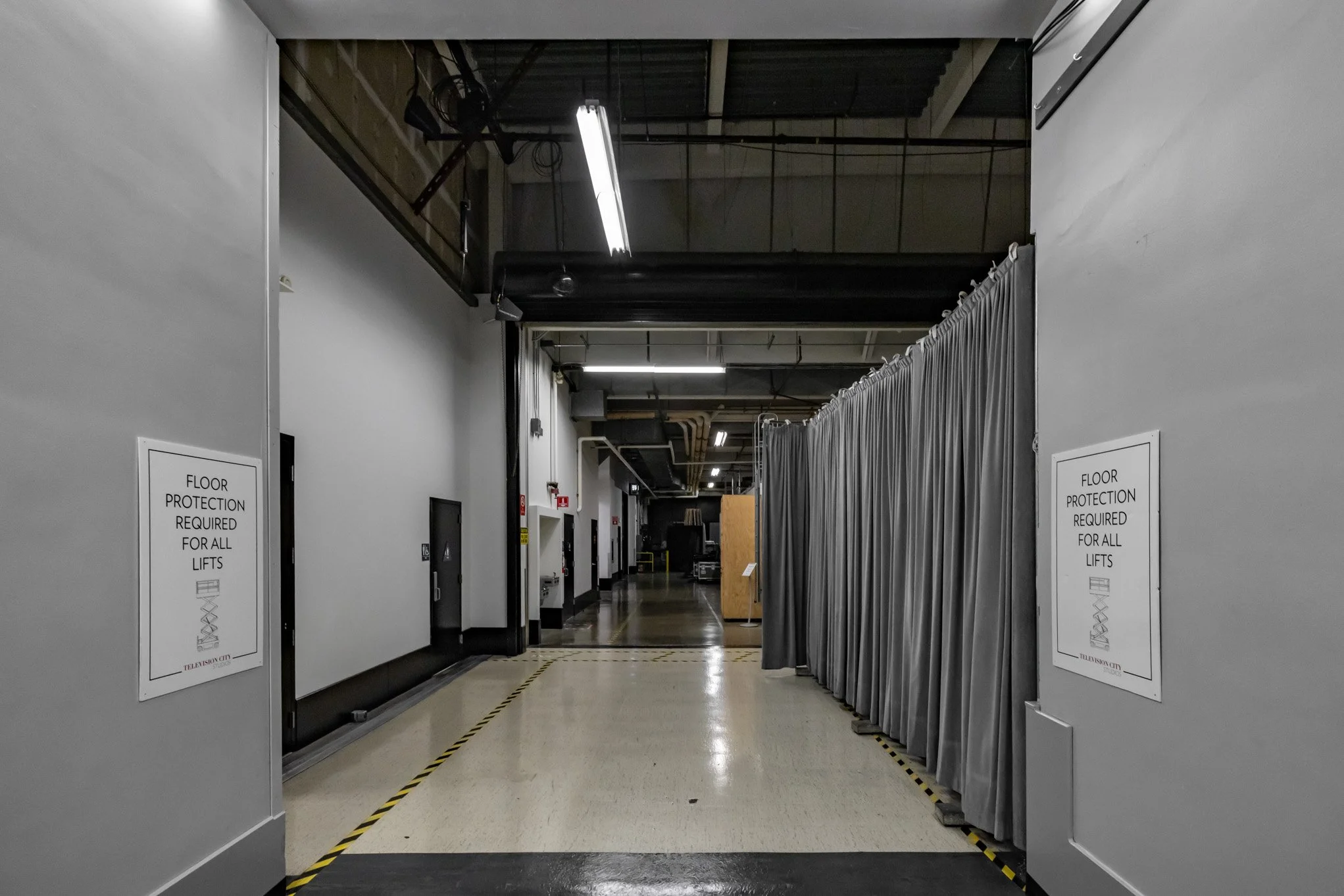 Indoor industrial space with a gray curtain divider, safety signs, and ceiling-mounted lighting fixtures.
