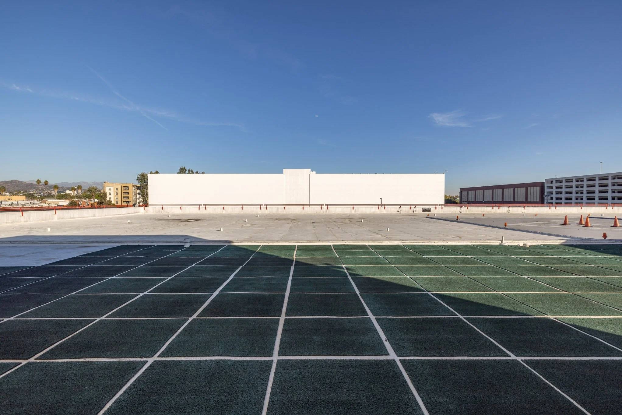 Empty rooftop parking lot with green painted parking spaces, orange cones, and a clear blue sky.