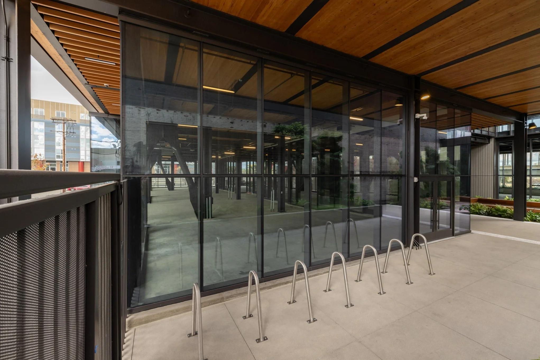 Modern building with large glass windows, metal bike racks outside, and wooden overhang, with a reflection of trees inside.