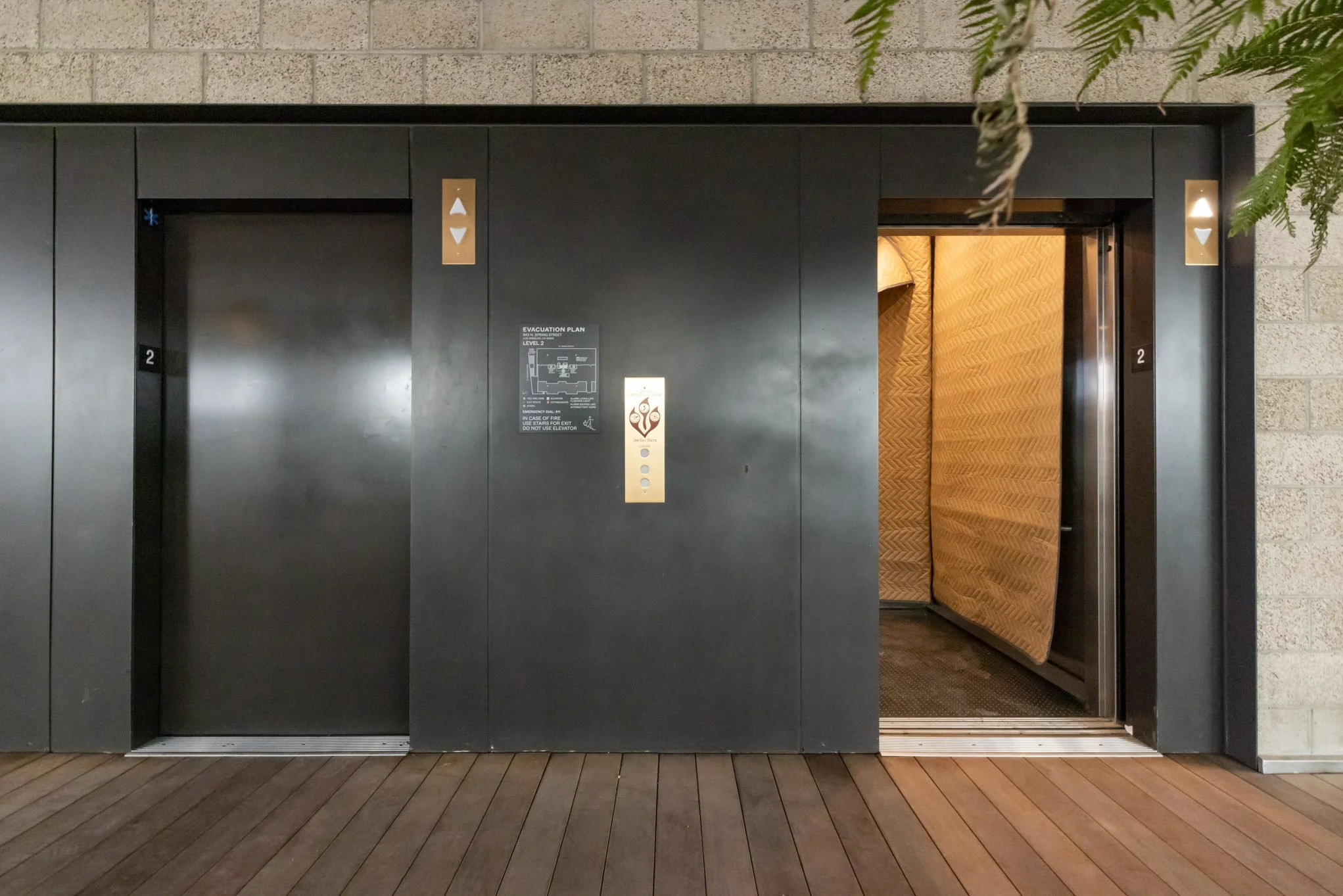 Elevator doors, one closed and one open showing an orange cushioned interior, in a building corridor.