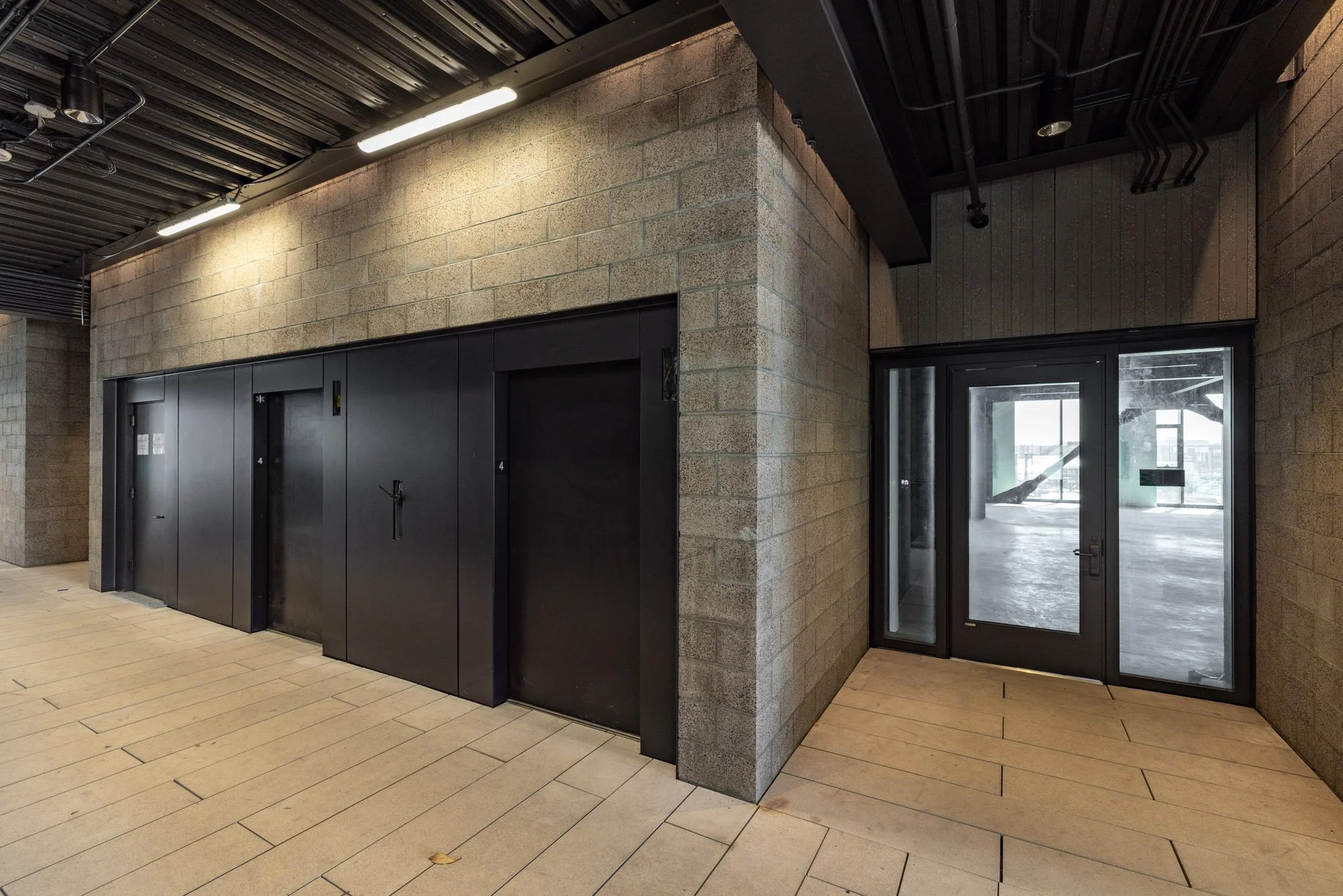 Interior of a modern building with black elevator doors, a glass door, and beige tiled flooring.