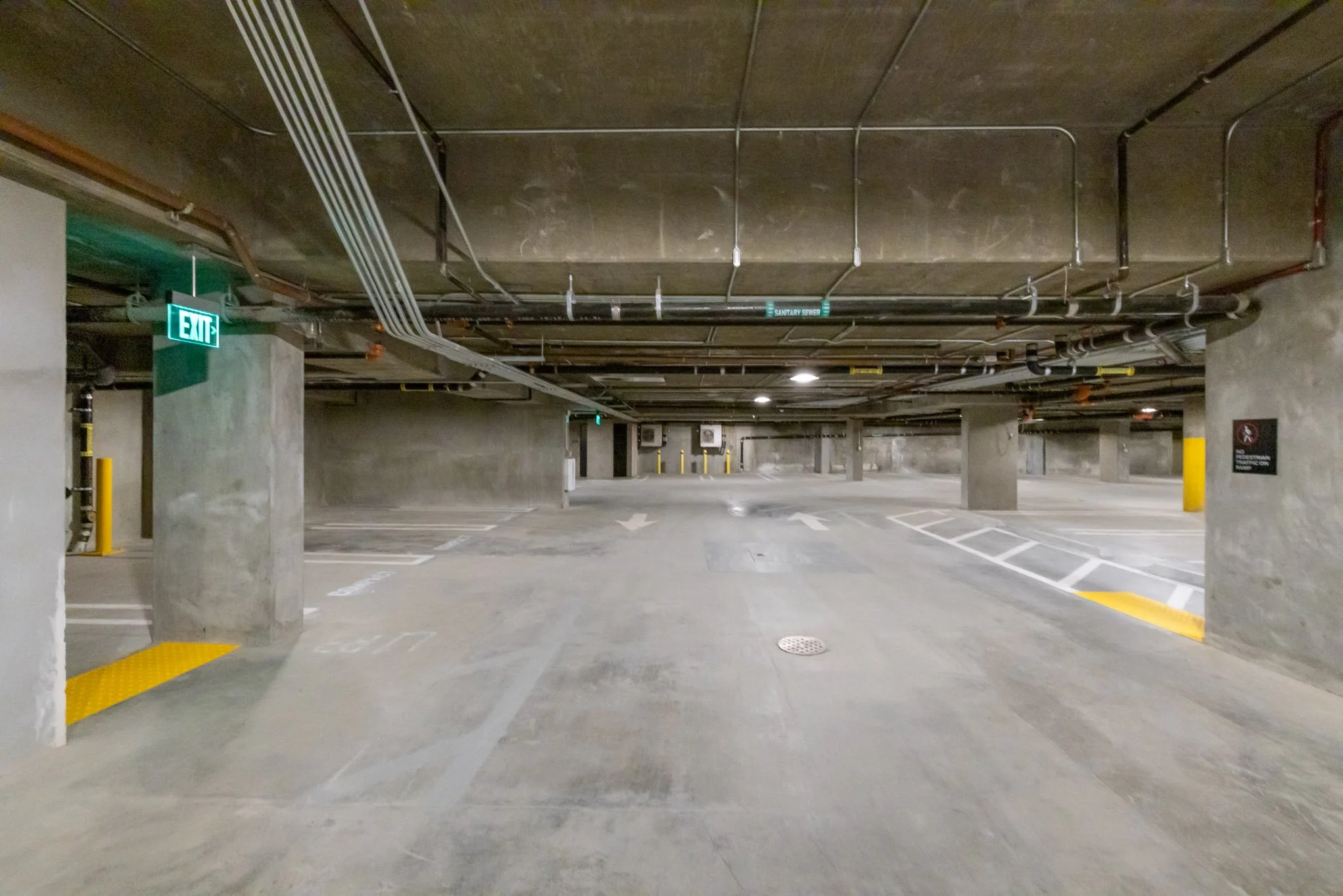 Empty multi-level parking garage with concrete columns, pipes, and marked parking spots.
