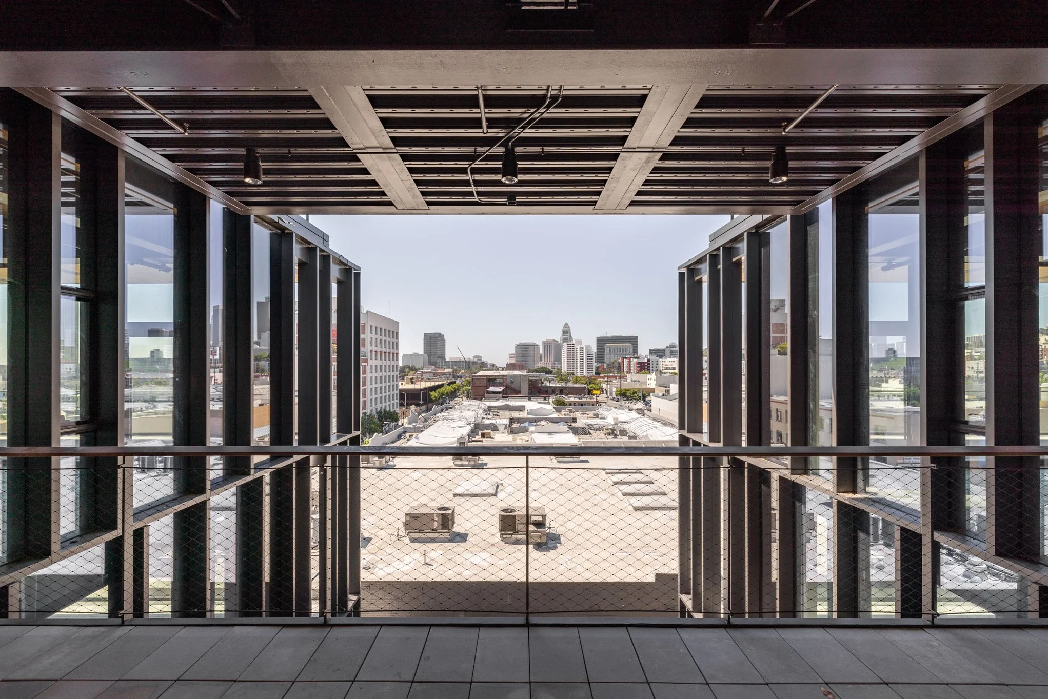 View of city skyline from a balcony with glass walls and a metal railing.