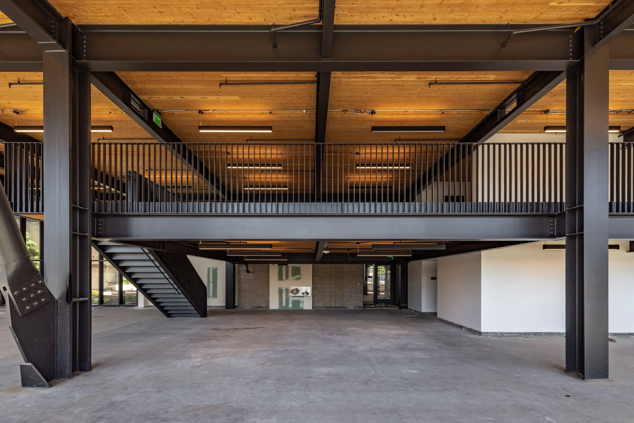 Interior of a modern industrial-style building under construction with exposed steel beams, a staircase, and a wooden ceiling.
