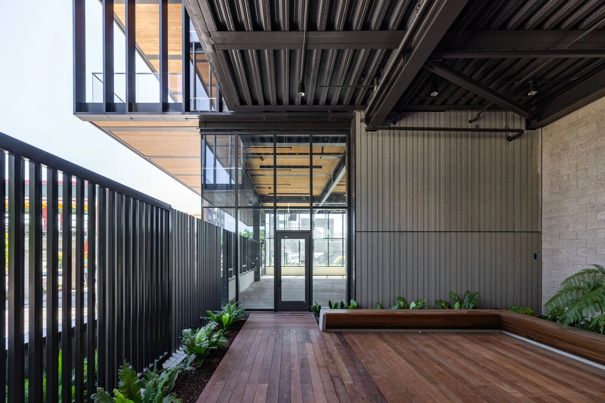 Modern balcony or patio area with wood flooring, black metal railing, glass walls, and some potted green plants.