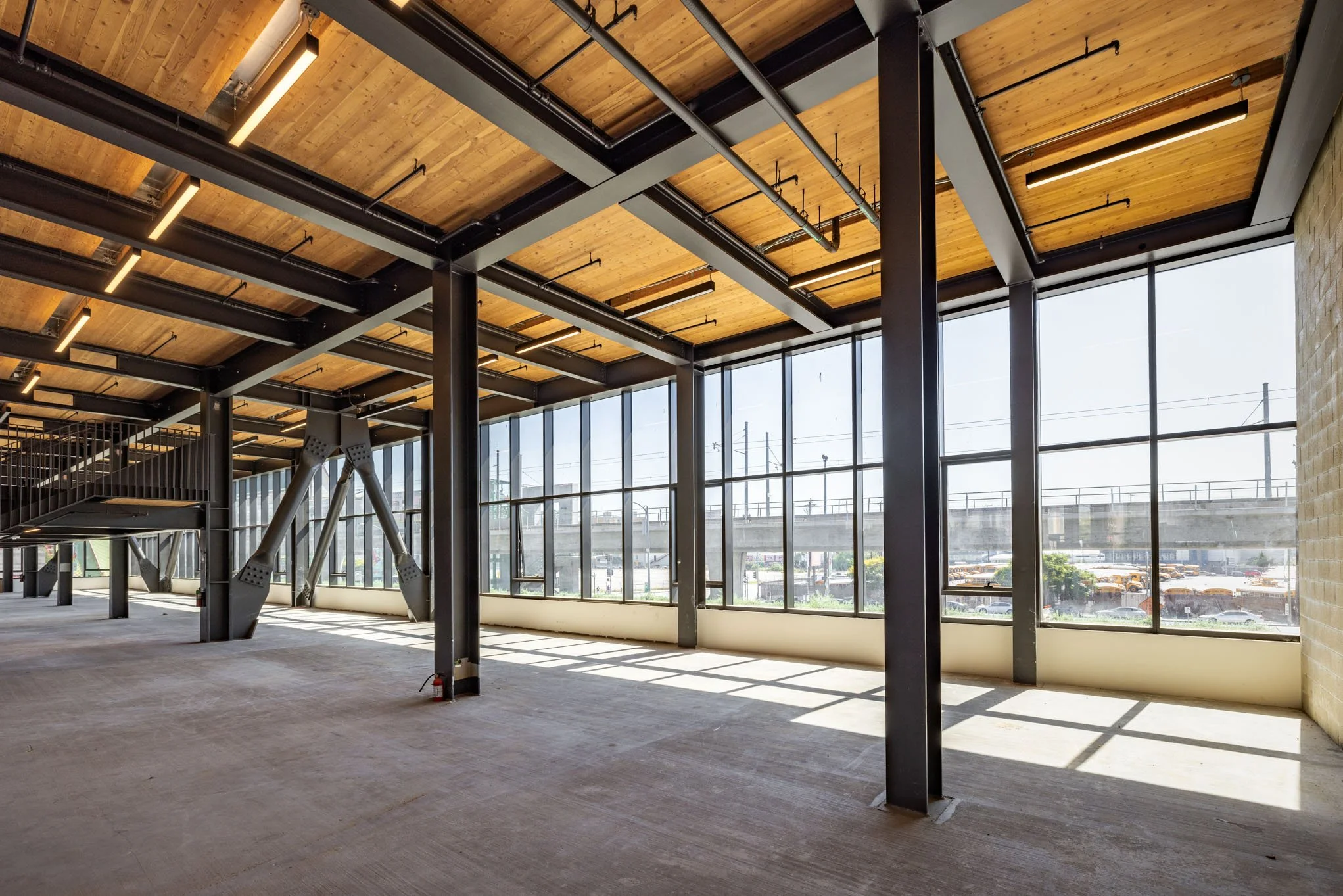 Empty commercial space with large windows, exposed brick wall, wooden ceiling, and metal support beams.