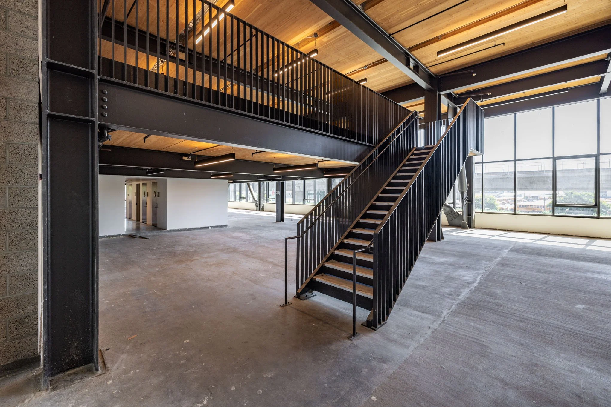 Empty indoor space with large windows, concrete floor, metal staircase, and wood ceiling in modern industrial style building.