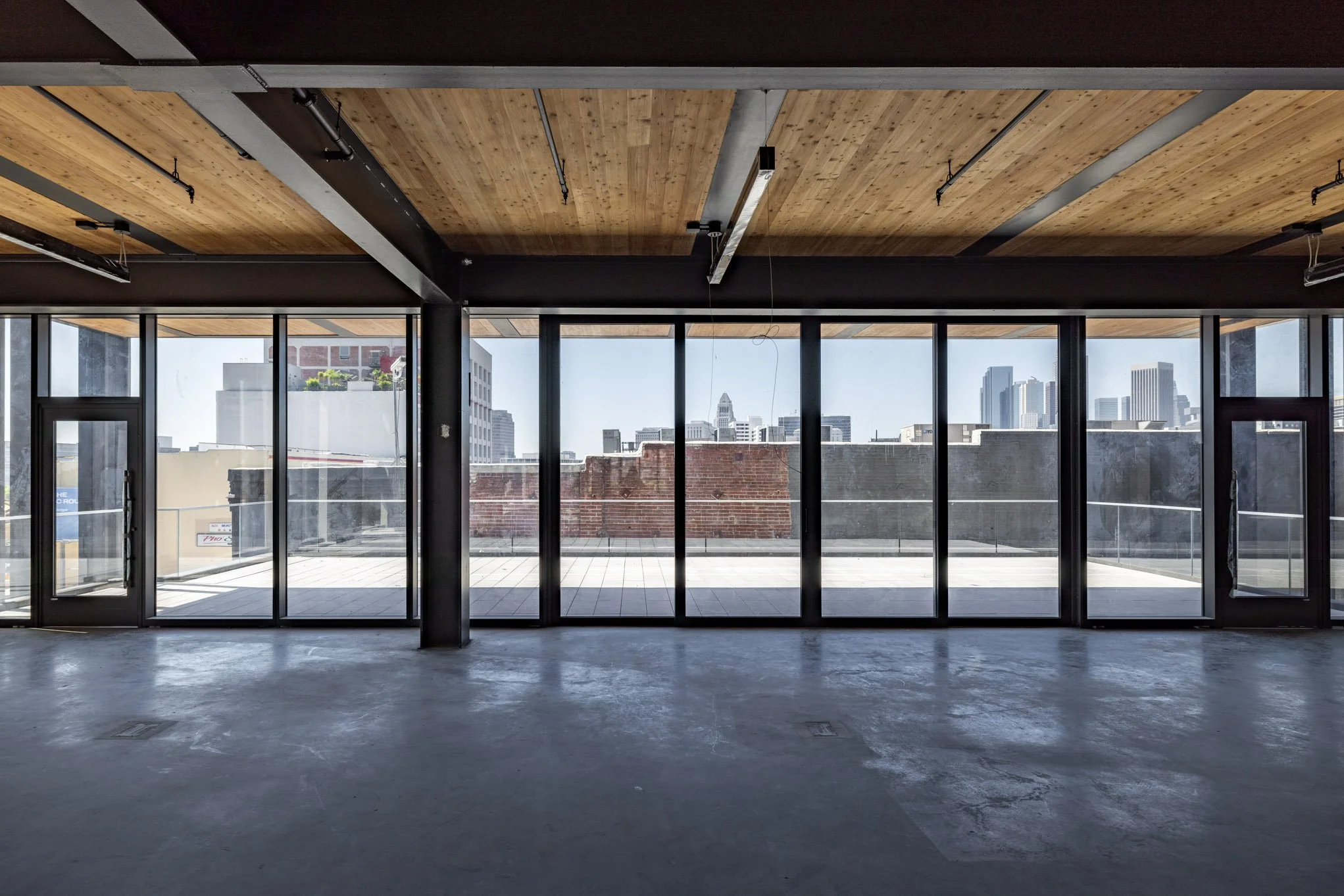 Empty interior space with large glass windows overlooking a city skyline with skyscrapers.