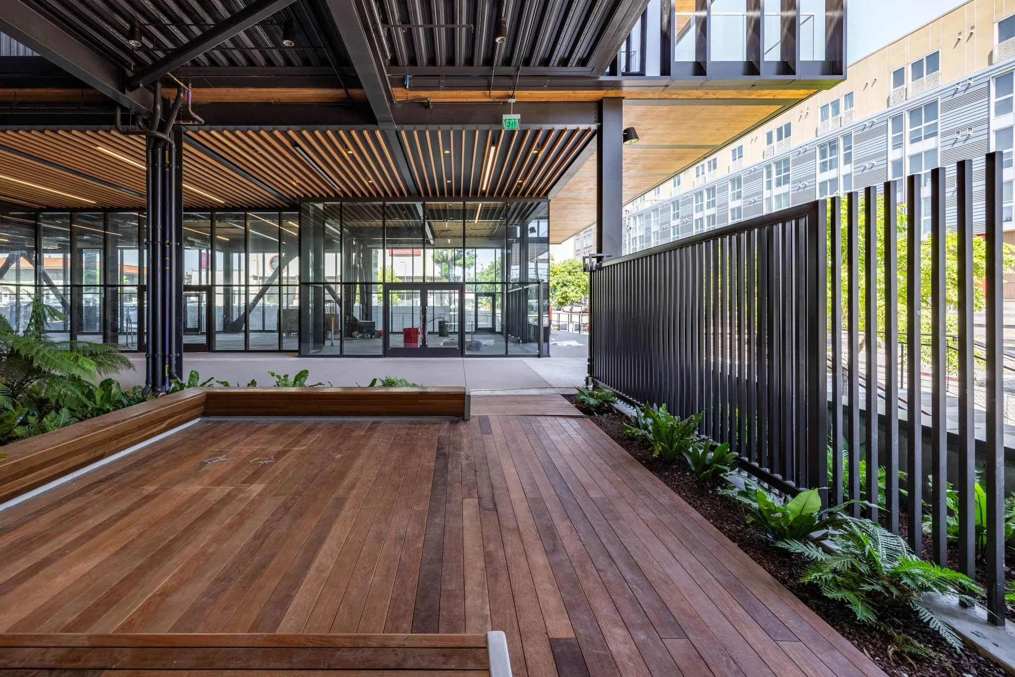 Modern building interior with wooden flooring, black metal fence, energy-efficient windows, and indoor plants.