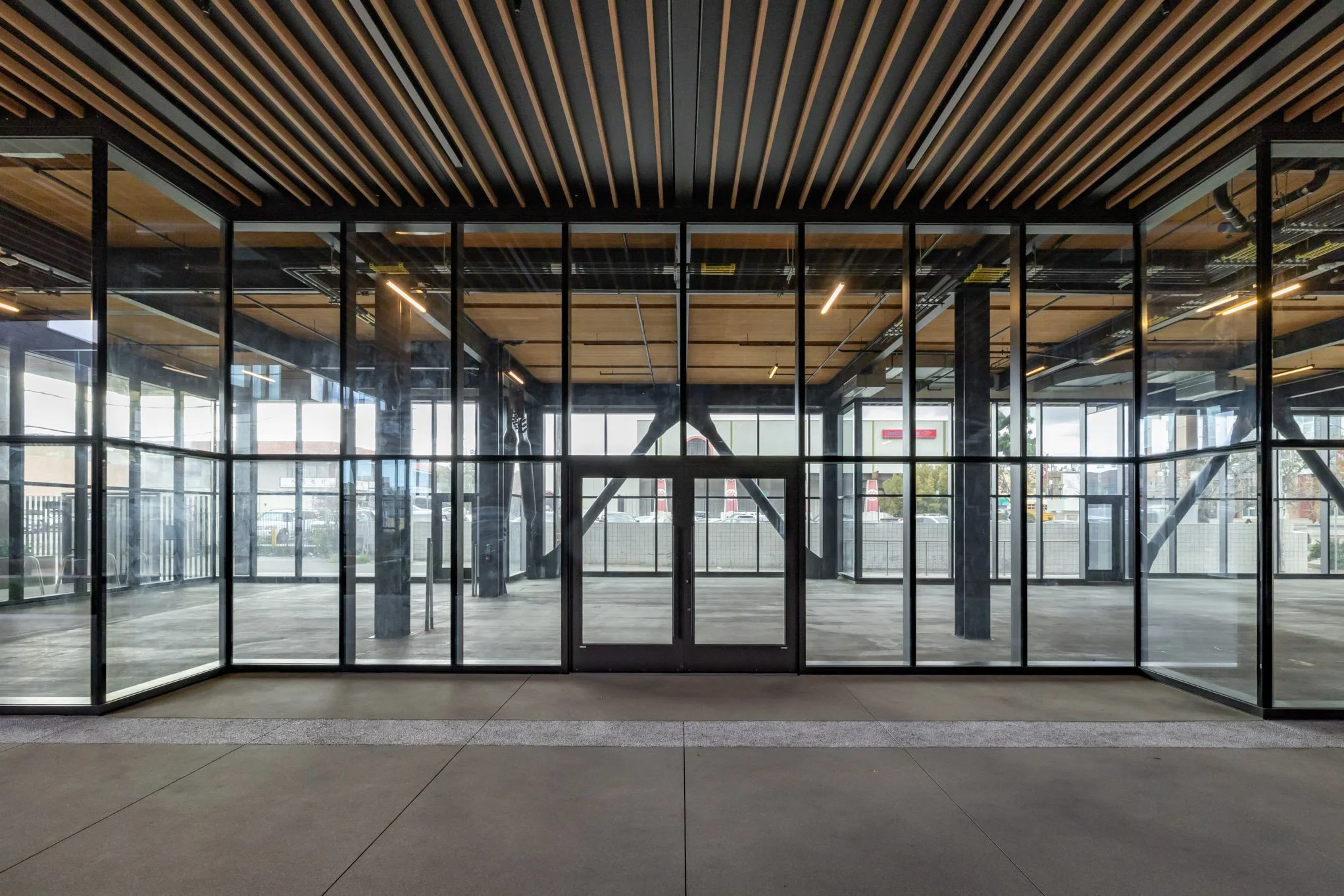 Empty modern lobby with glass walls, black metal framework, and wooden ceiling panels.