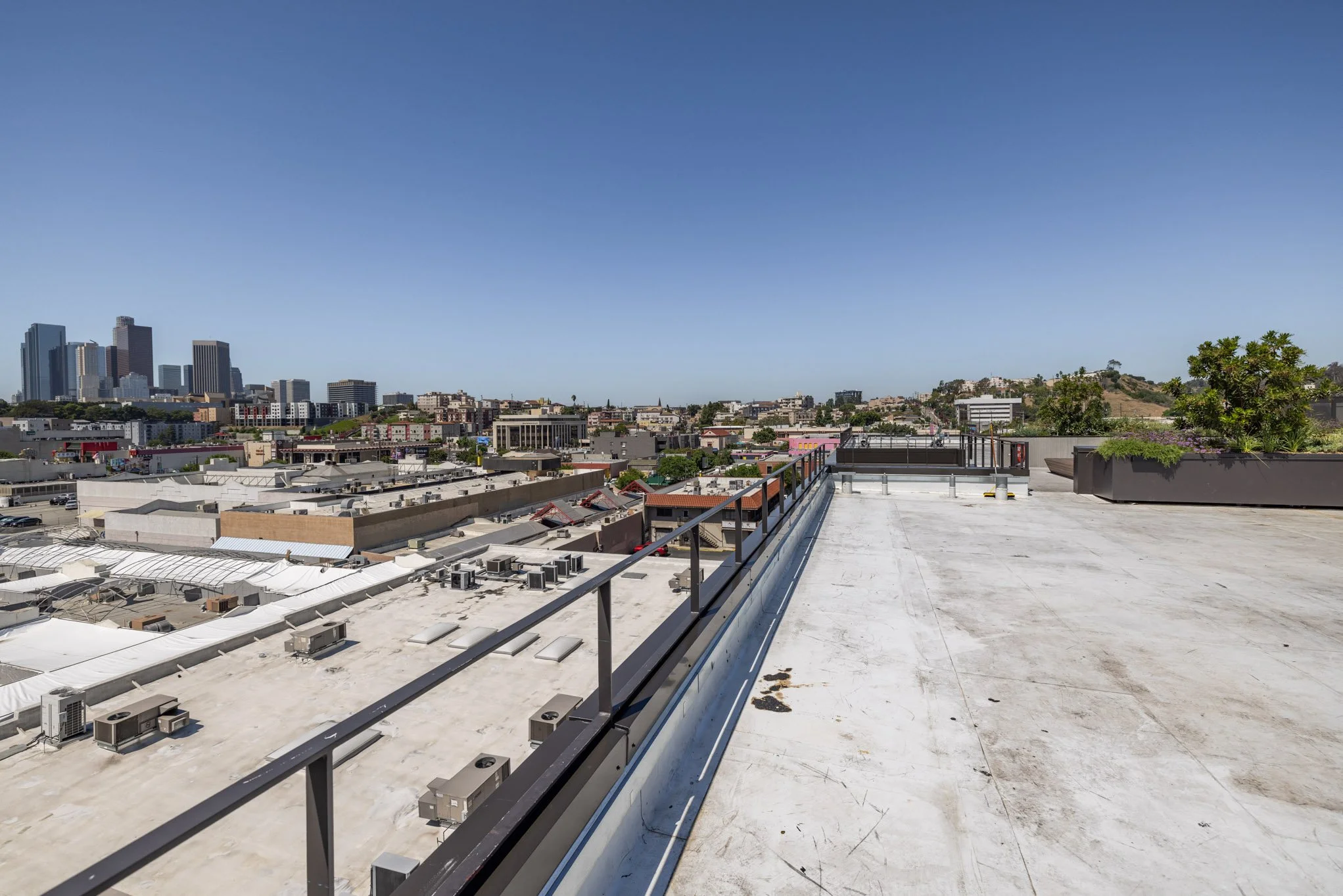 Empty rooftop with planters and city skyline in the background under a clear blue sky.