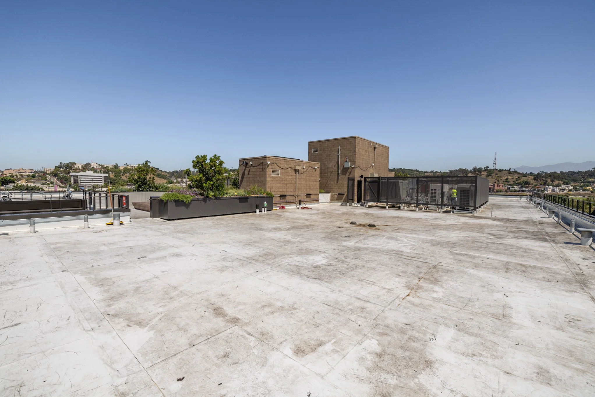 Empty rooftop with a view of some buildings and hills in the background, clear blue sky overhead.