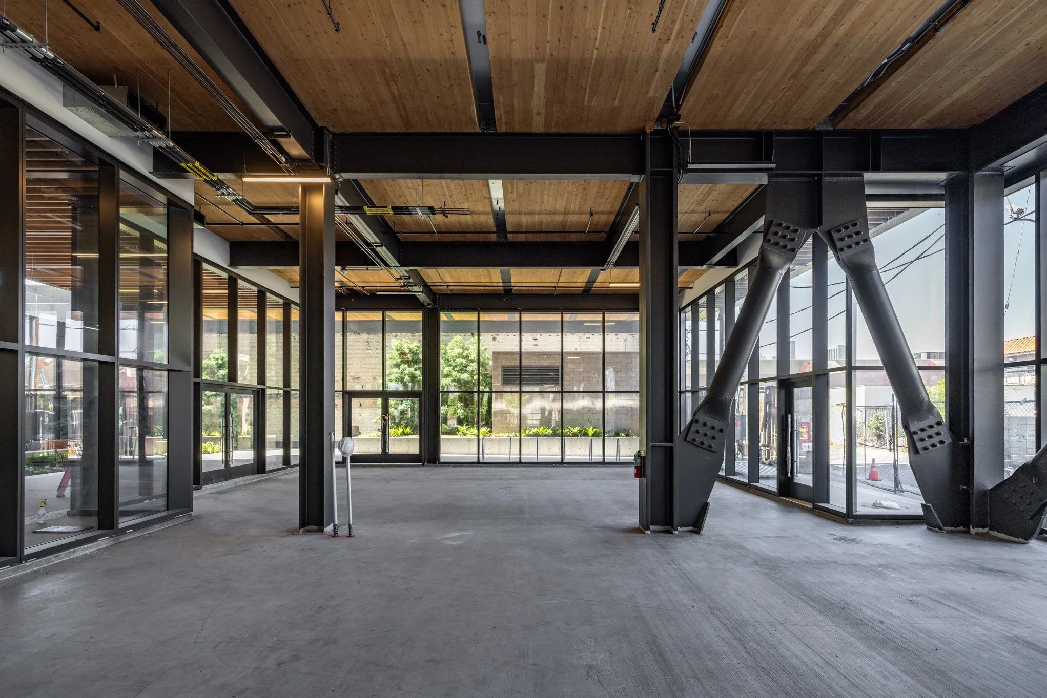 Empty modern interior space under construction with large glass windows, metal beams, and a partially installed ceiling.