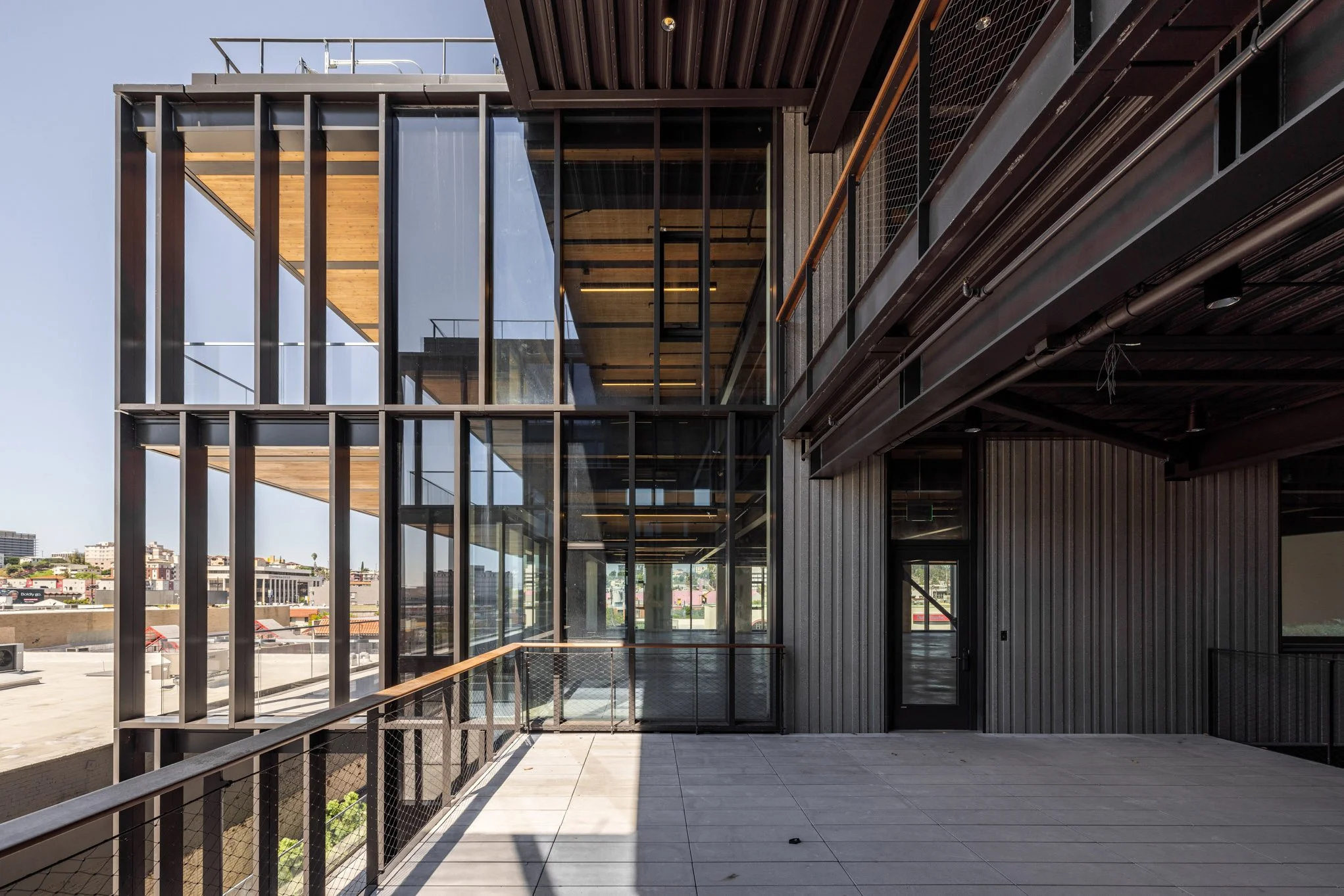 Modern building with glass windows and metal framework, including a balcony with a metal railing, overlooking a cityscape.