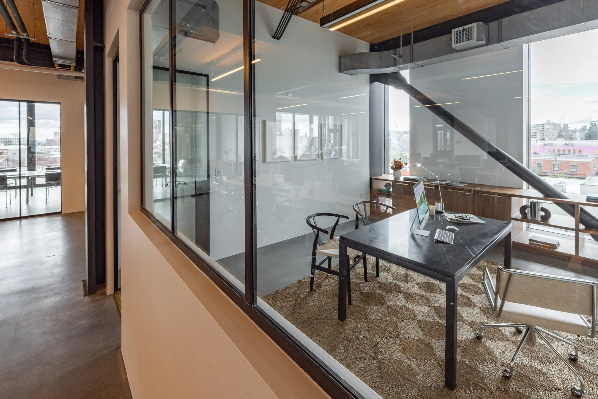 Office with large windows, black desk with computer, two chairs, and a beige and brown patterned rug.