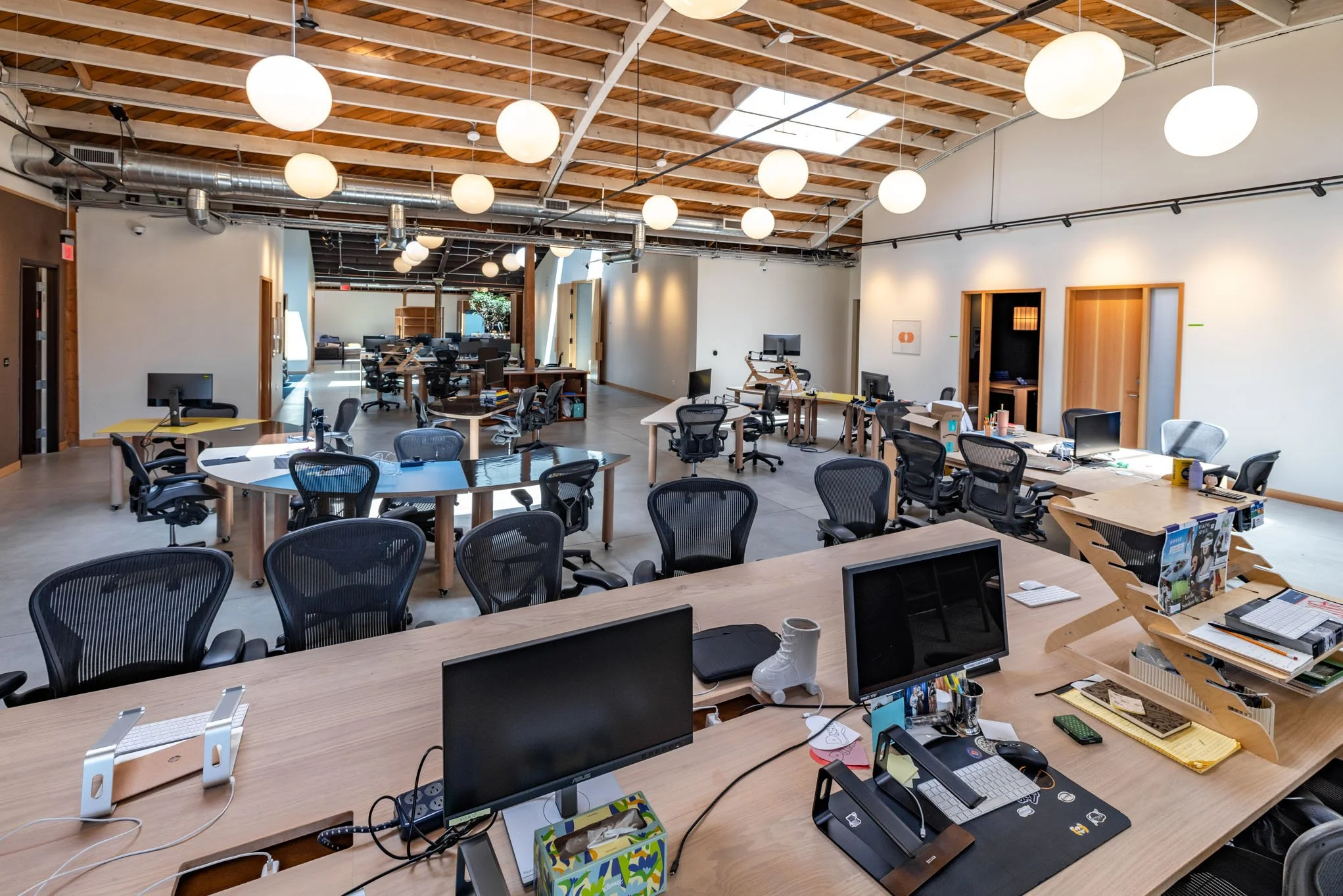Open-plan modern office with desks, chairs, computers, and lighting fixtures.