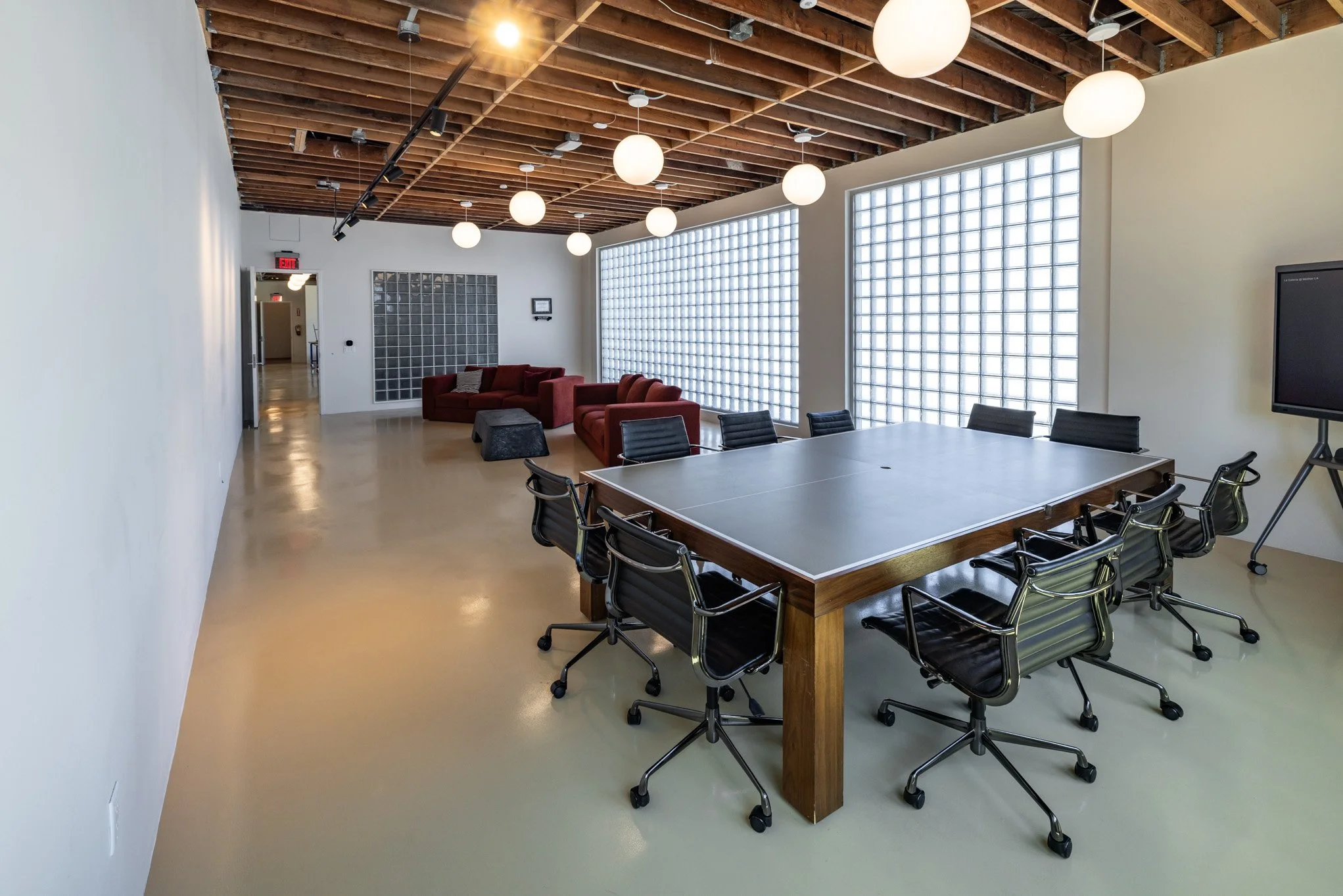 Modern conference room with a large table, black chairs, red couches, and decorative lighting fixtures.