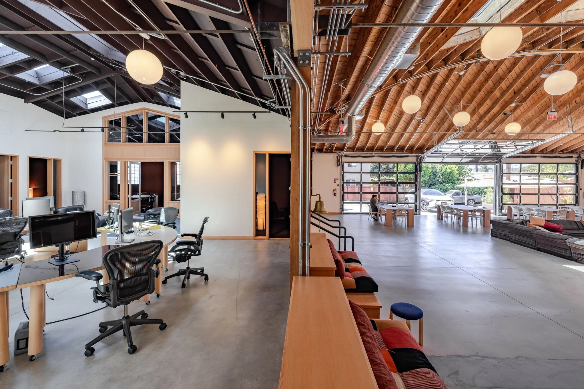 Spacious modern open-plan office and lounge area with high wood vaulted ceiling, large windows, workstations, and seating arrangements.