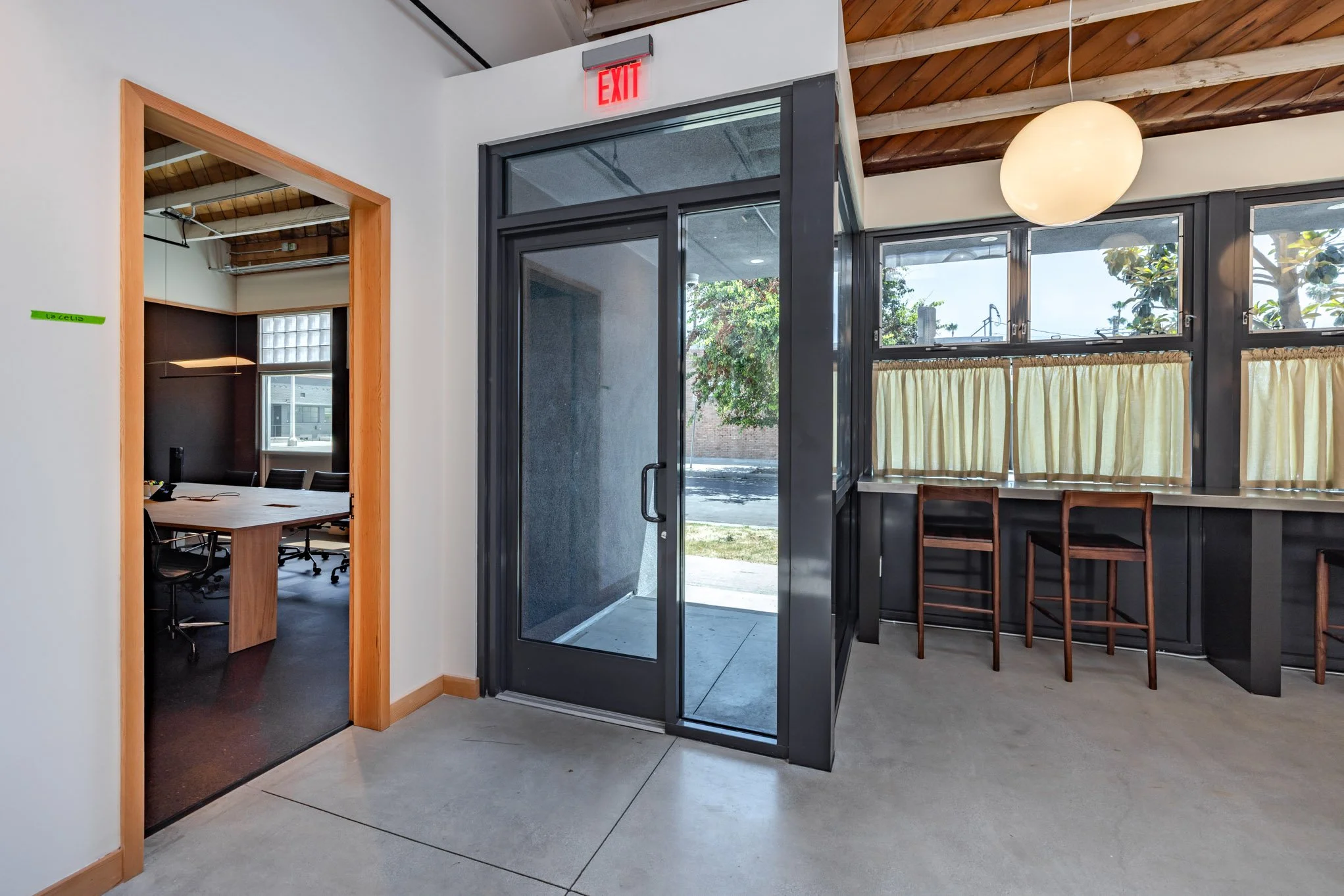 Interior of a modern office space with a hallway, glass door, window seating area with yellow curtains, and a conference room visible through an open door.