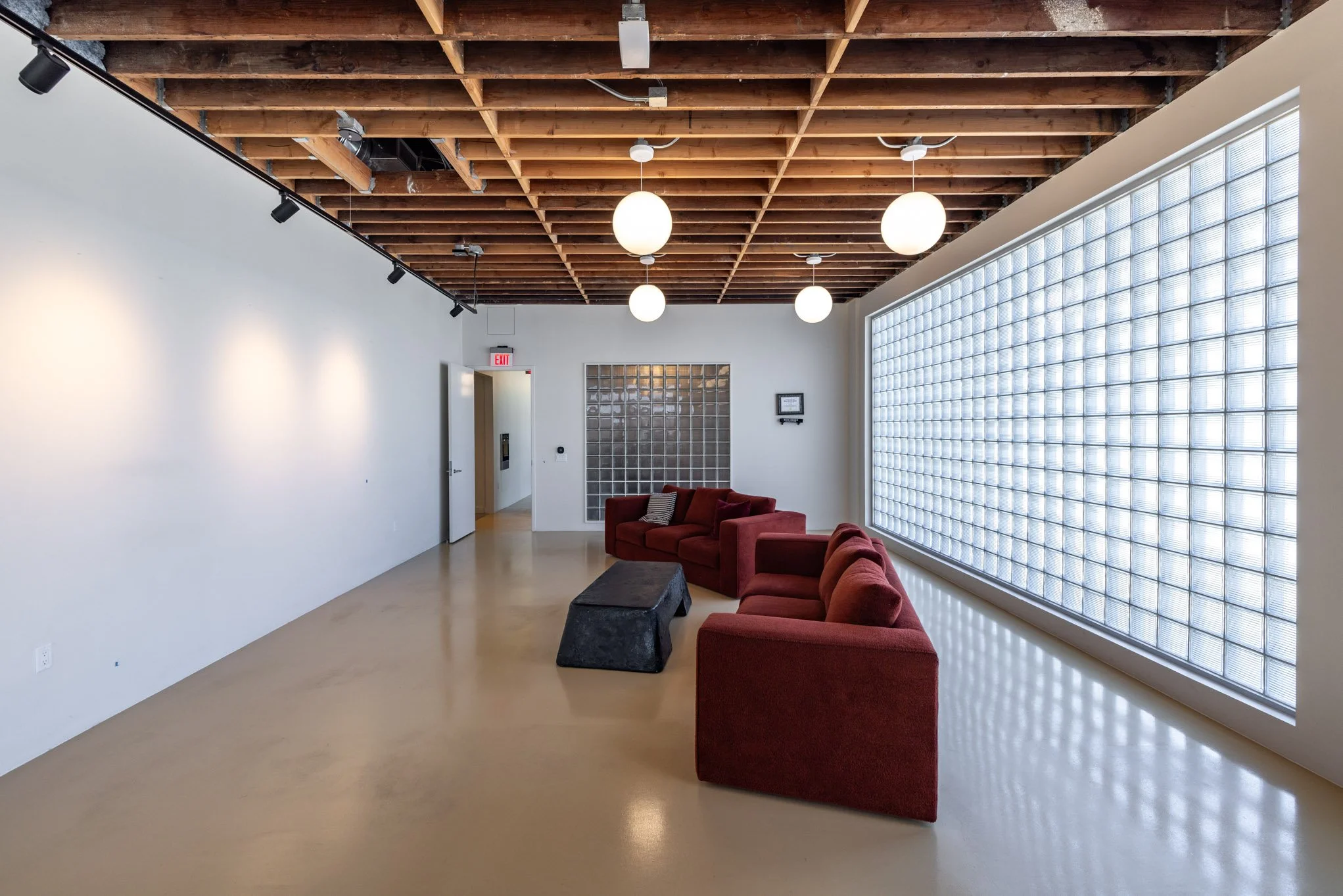 Modern lounge with red sofas, black ottoman, white walls, glass block window, wooden ceiling, and globe pendant lighting.